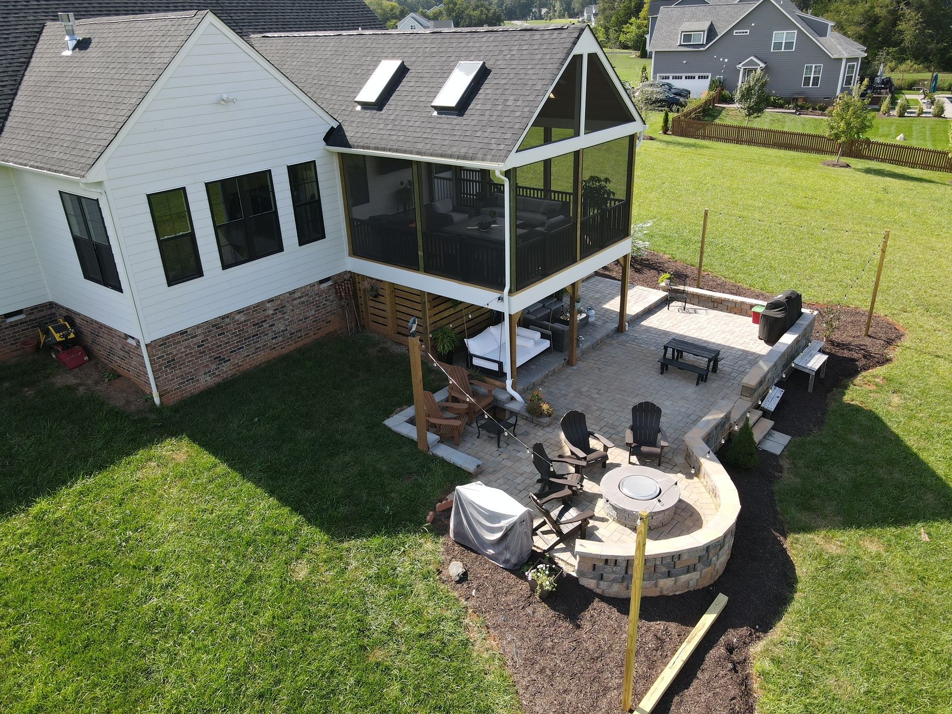 Aerial view of a white house with a screened porch and patio seating on a large green lawn.