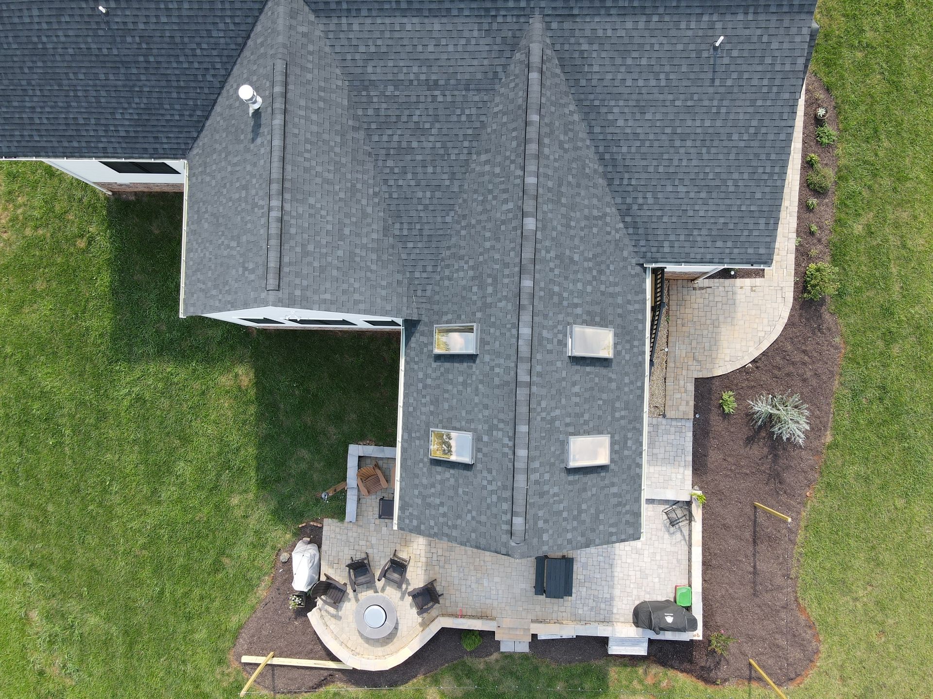Aerial view of a house roof, patio, and surrounding green lawn and landscaping.
