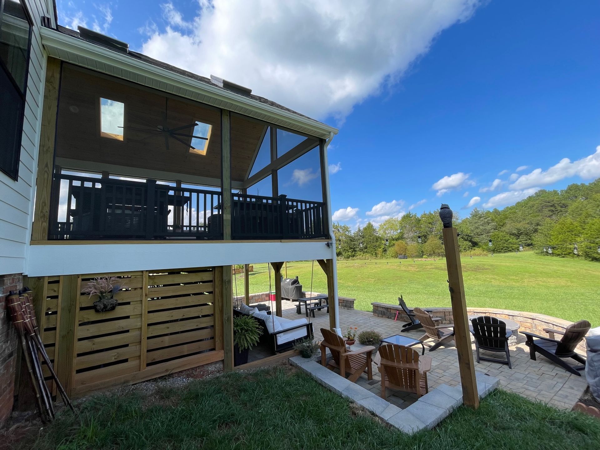 Covered outdoor patio beside a grassy yard and pool, with lounge chairs, fire pit, and blue sky.