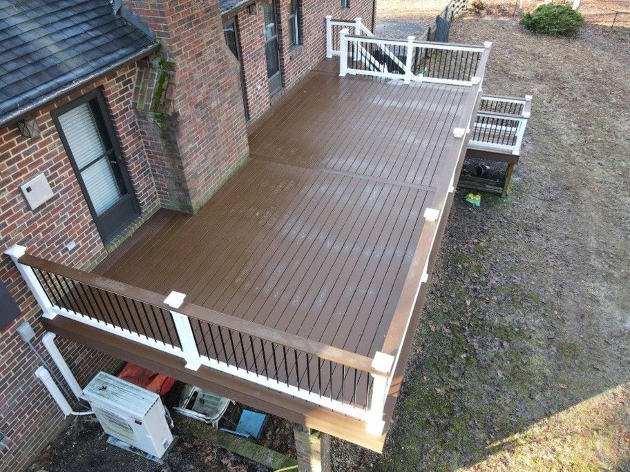 Wooden deck beside a brick house with white railing and steps leading to a gravel yard.