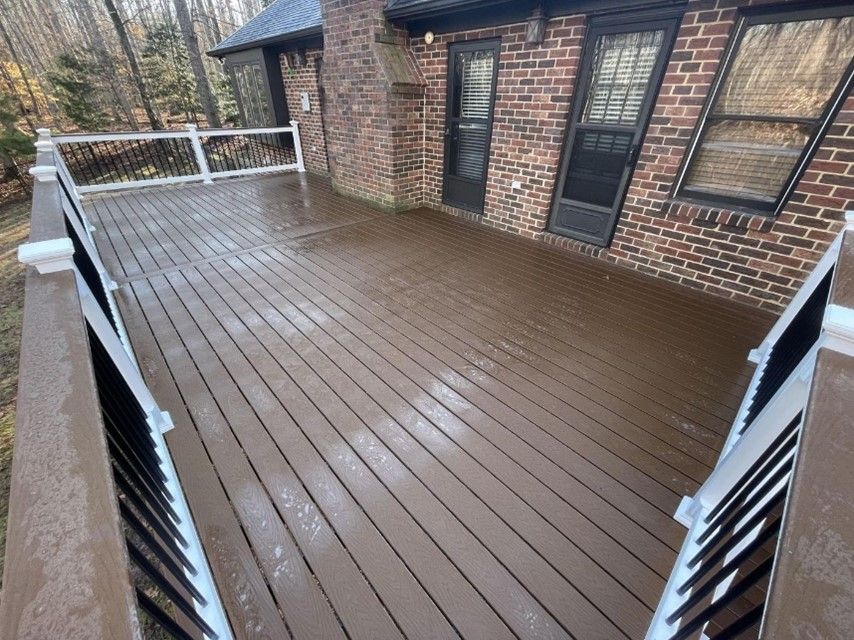 A spacious wooden deck with black and white railings attached to a brick house with trees Wet wooden deck beside brick house with white railing and stairs