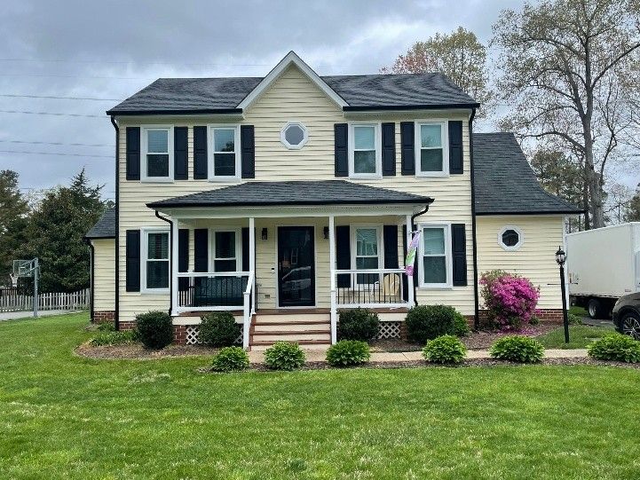 A cream-colored two-story house with black shutters, a covered front porch, and landscaped lawn.