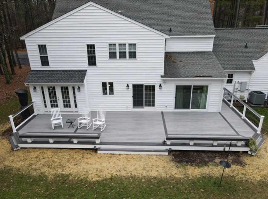 Rear view of white house with large deck and outdoor chairs.