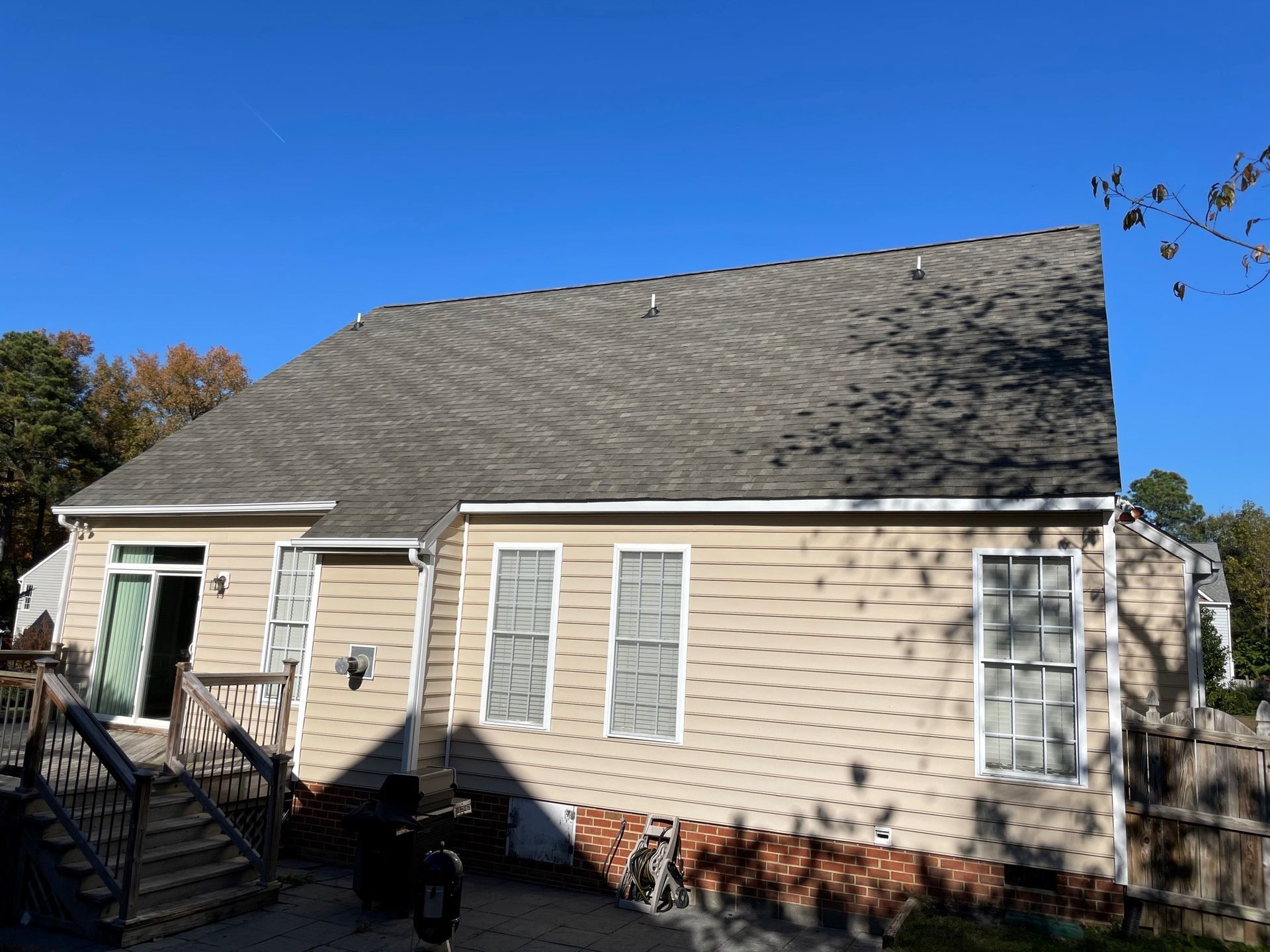 Beige house exterior with gray roof, white shutters, stairs, and autumn trees under a blue sky