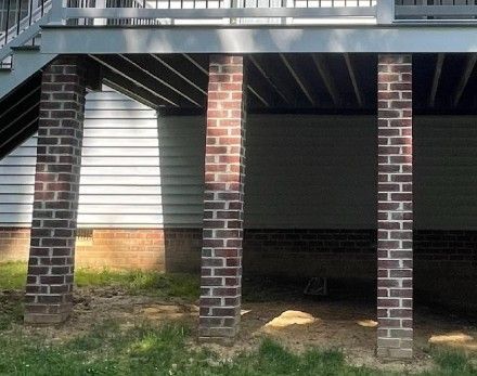 Brick pillars supporting an elevated deck beside a house, with shaded space underneath and grass below