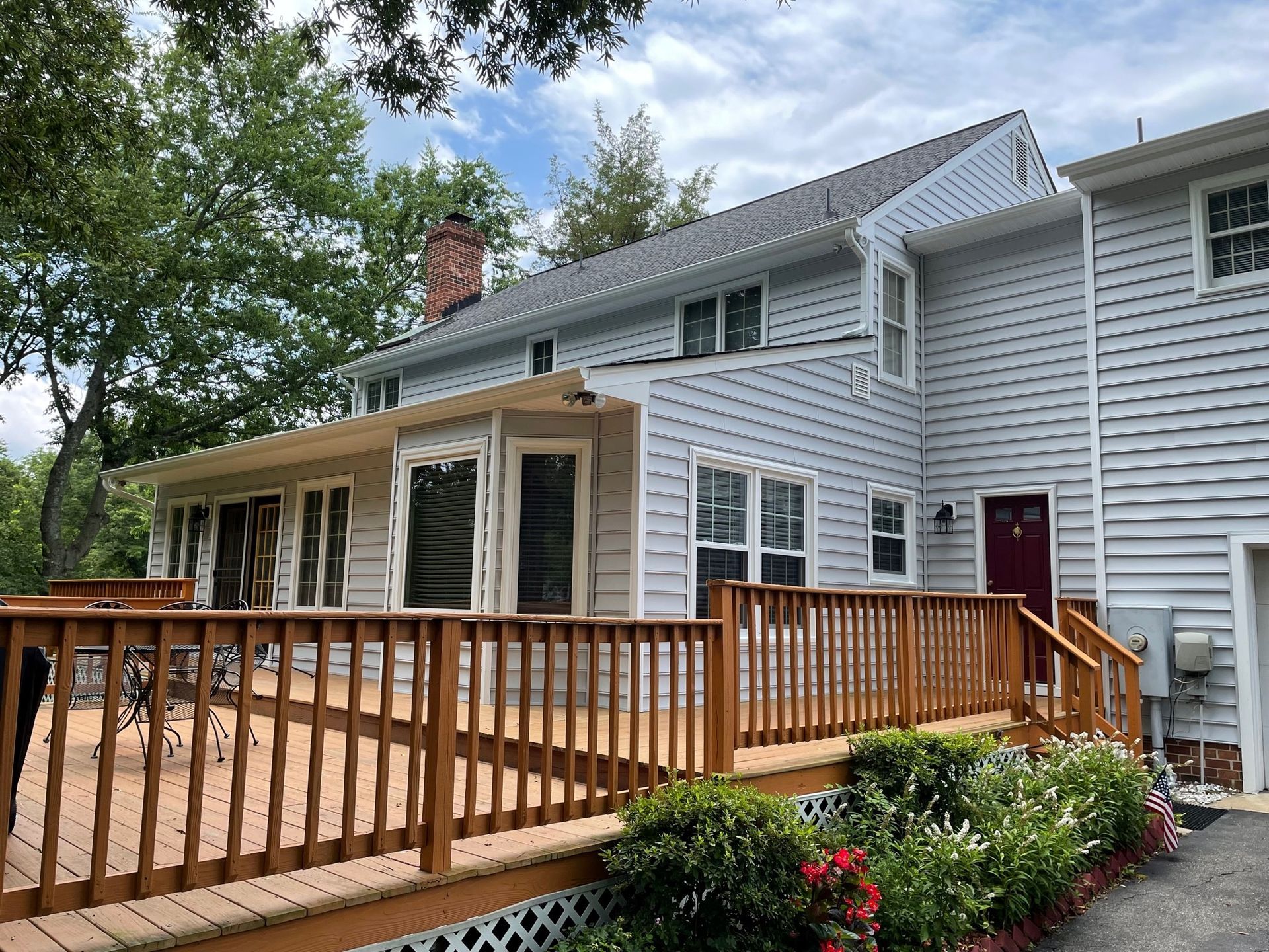 Wooden deck beside a gray two-story house with white trim and a red door, viewed from the backyard.