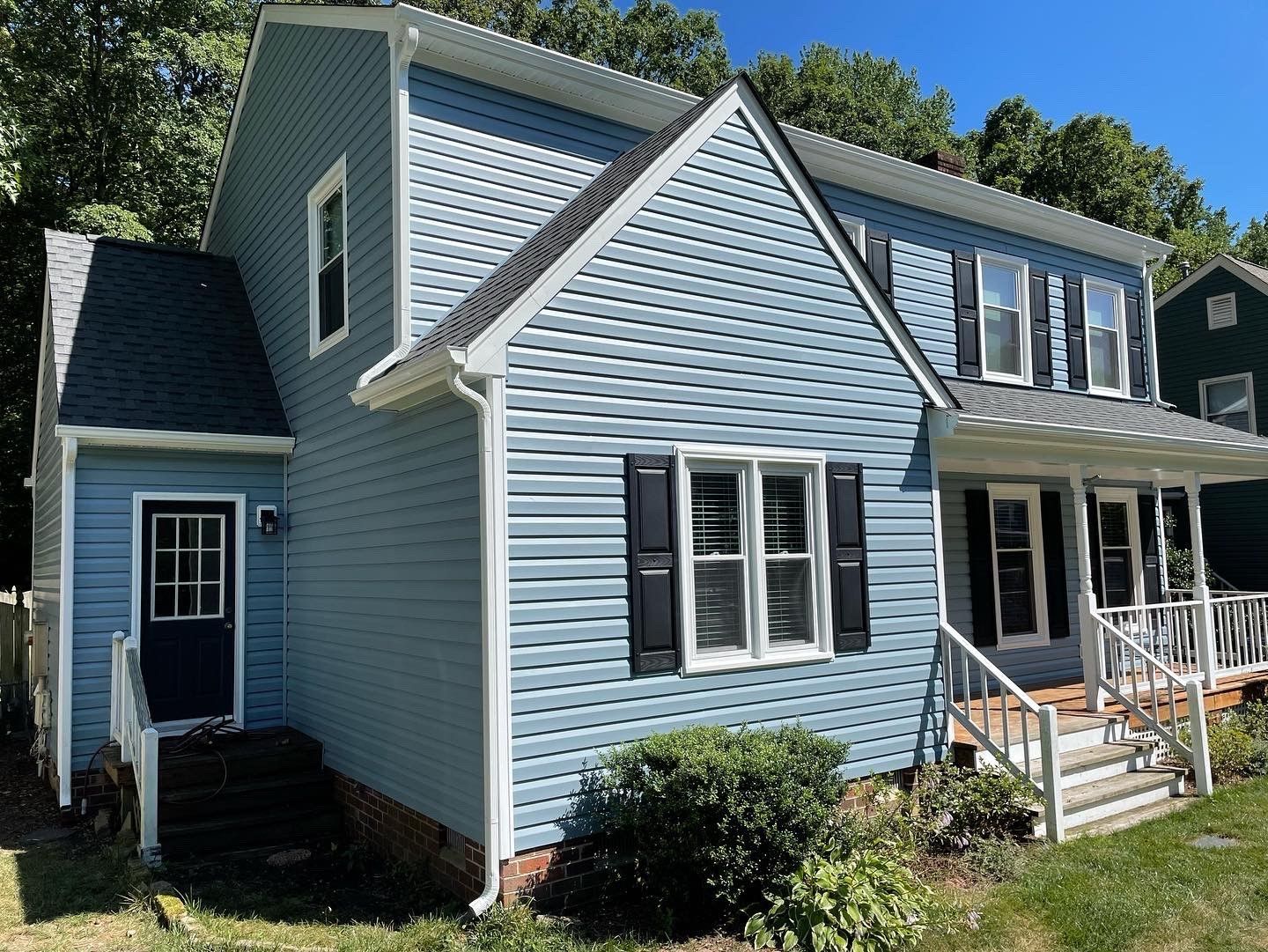 Blue two-story house with white trim, front porch, and attached side addition in a wooded setting