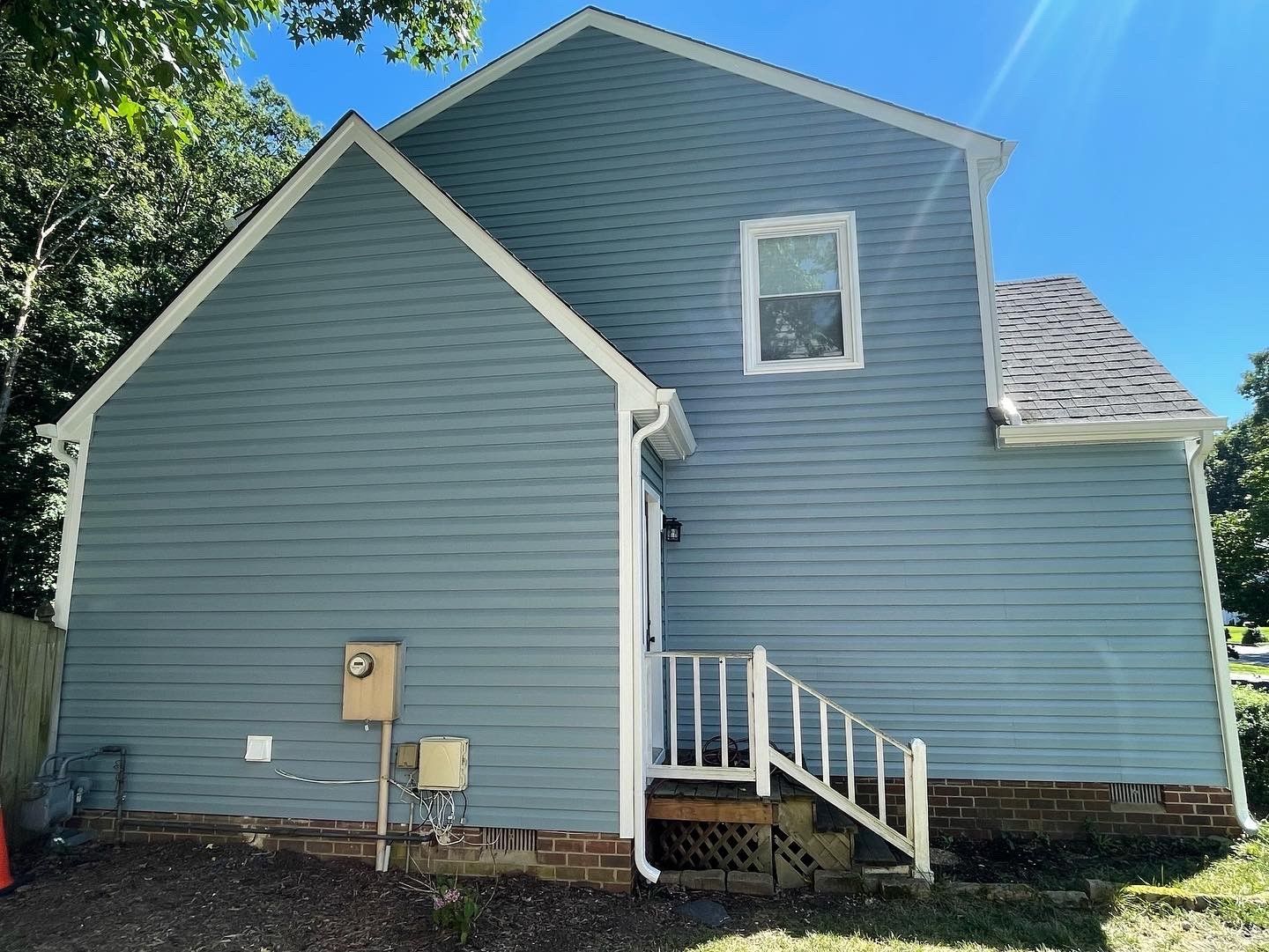 Blue house exterior with white trim, small porch steps, and a window under a gabled roof.