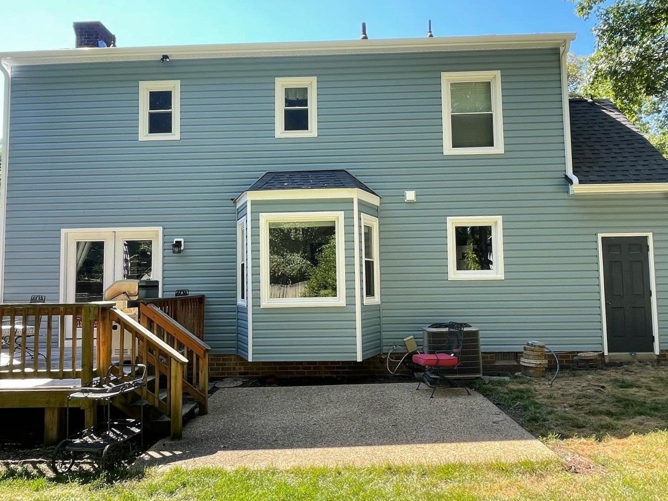 Blue house exterior with a small wooden deck, central doorway, and gravel walkway.