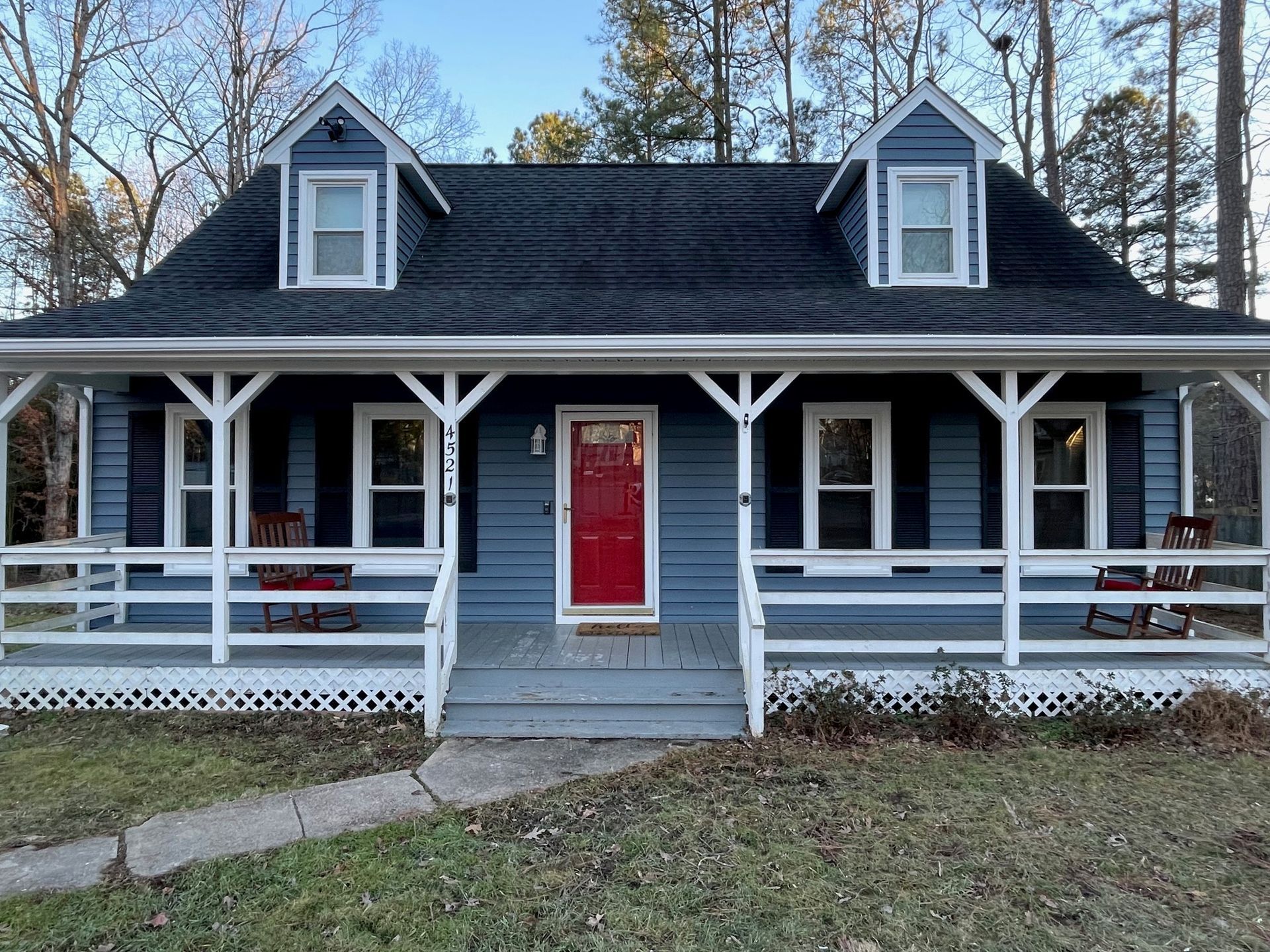Blue house with white porch and red front door, viewed from the front yard