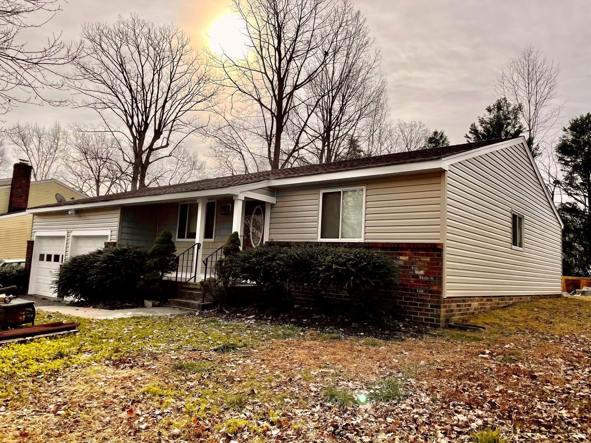Single-story house with beige siding, front porch, and leaf-covered yard under bare trees in autumn.