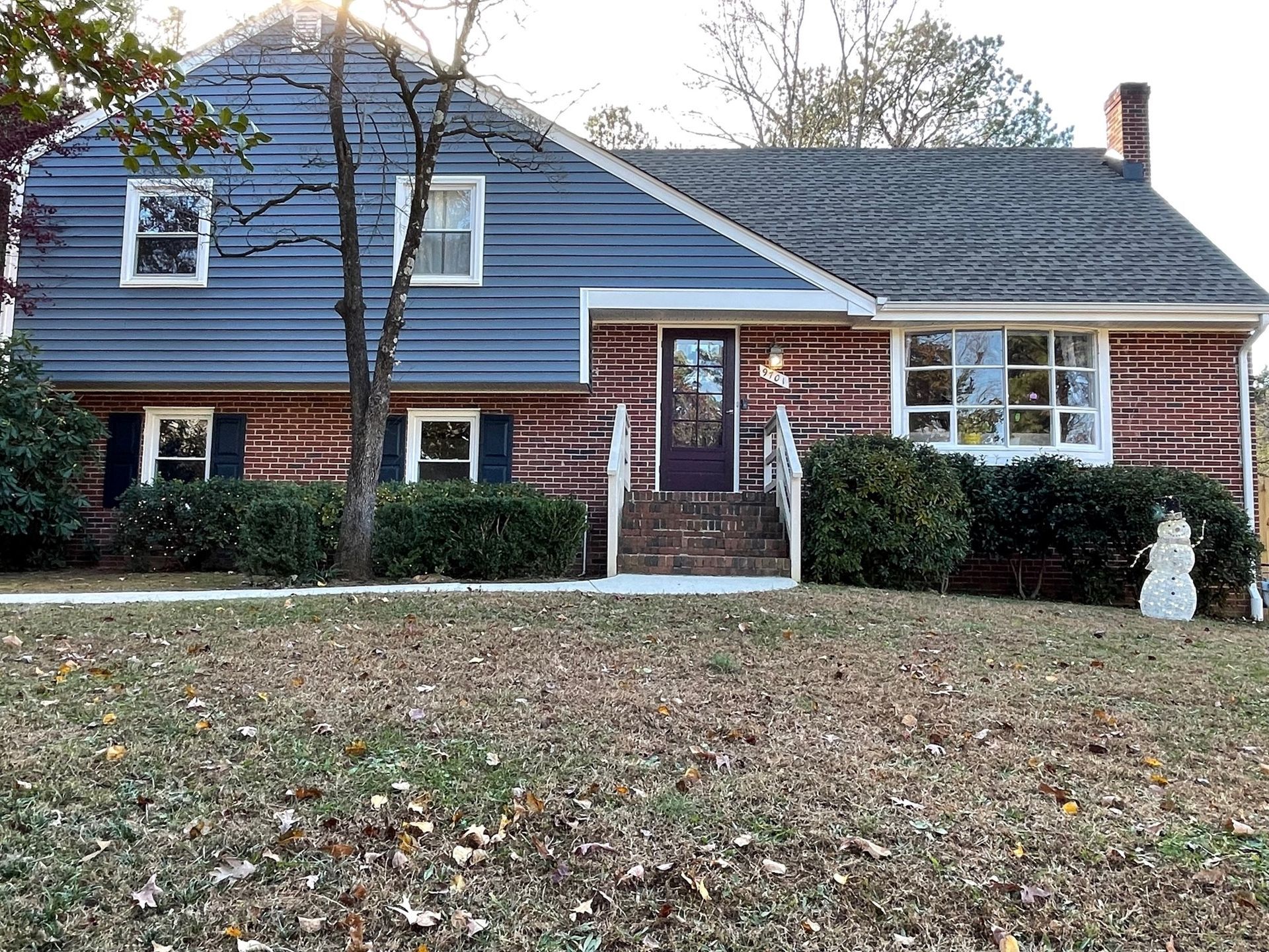 Blue-and-brick suburban house with a front lawn, shrubs, and a front door centered under a gabled roof