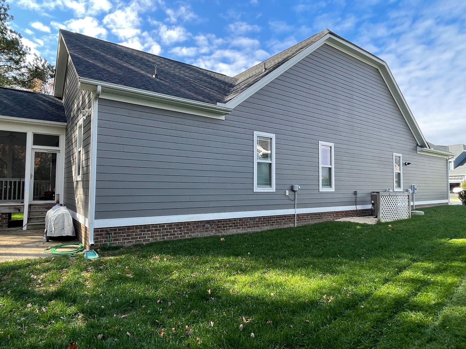 Gray house exterior with white trim, brick foundation, and green lawn under a blue sky
