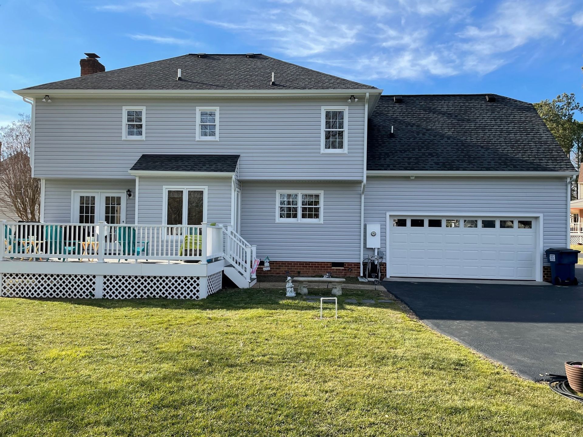 Two-story white house with a front porch, garage, and green lawn under a blue sky