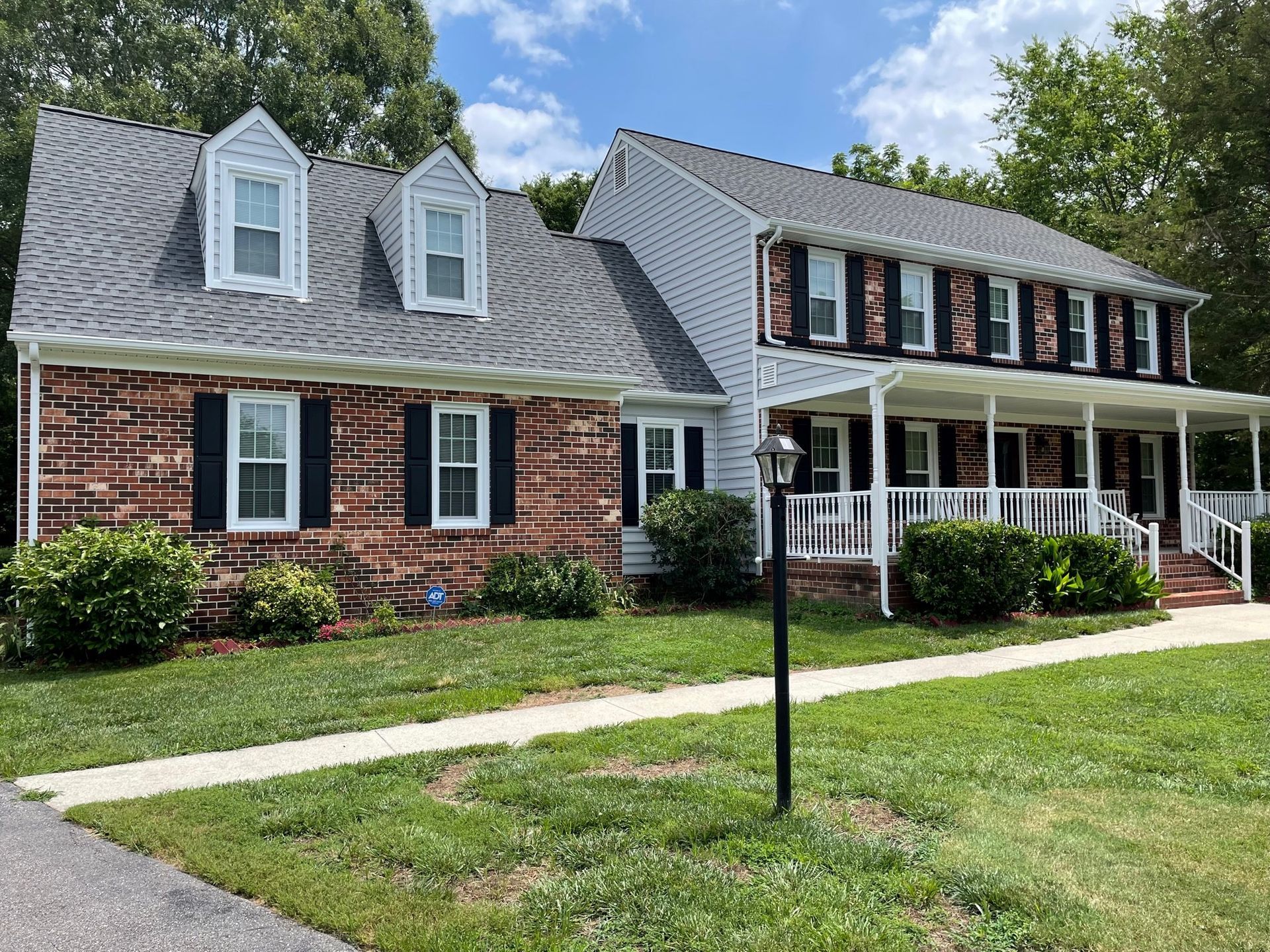 Brick house with dormers and porch, set on a green lawn under a blue sky