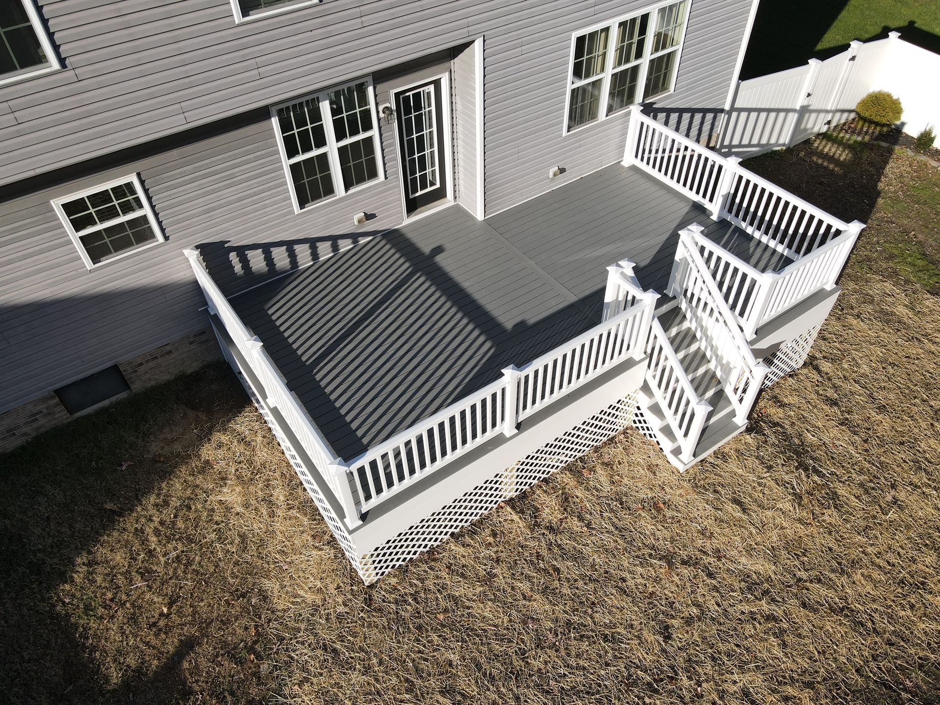 Back porch deck with white railings, gray flooring, and stairs beside a house
