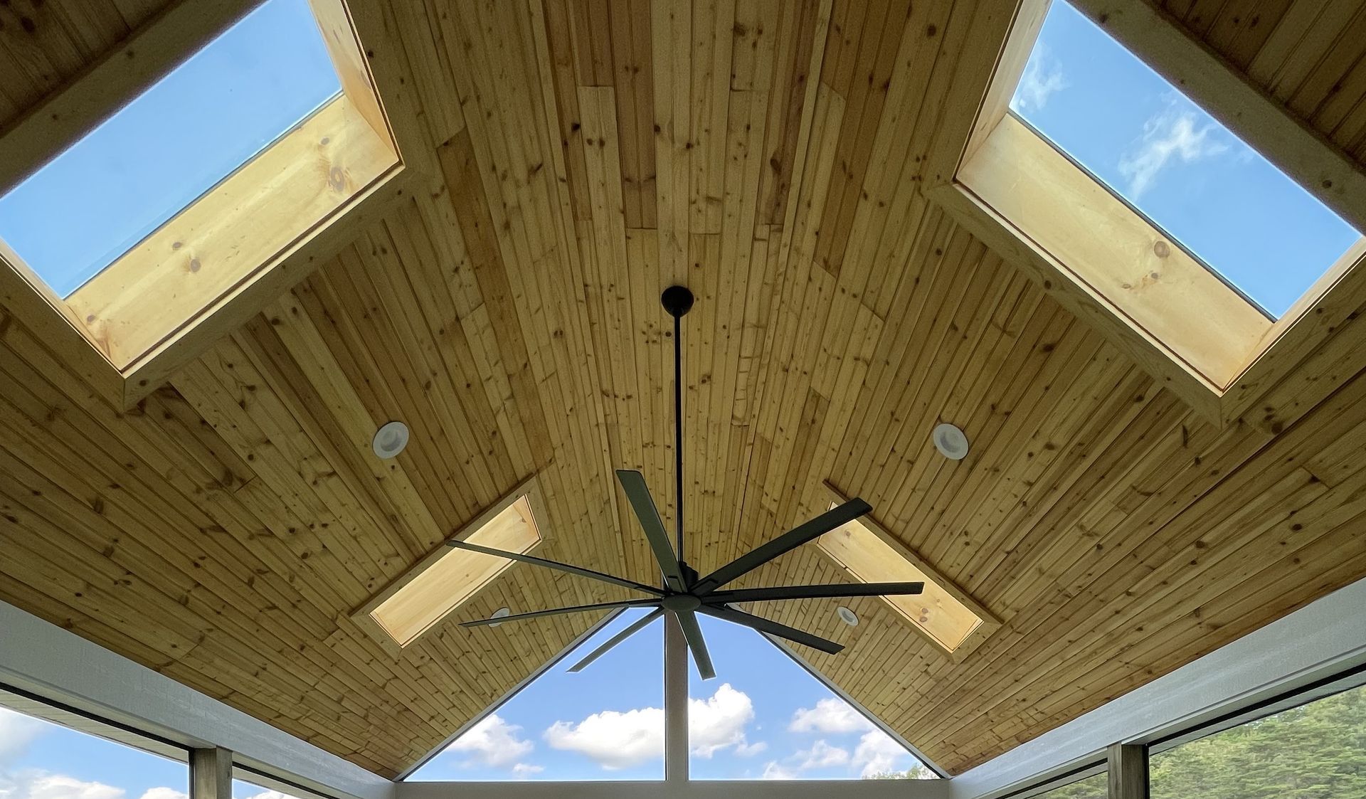 Wood-paneled vaulted ceiling with skylights and a black ceiling fan above a bright room