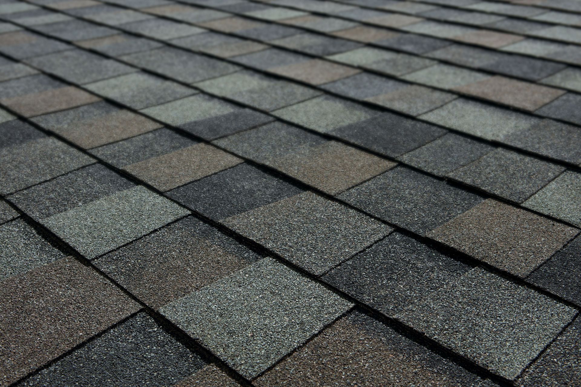 Close-up of overlapping gray and brown roof shingles with a textured pattern