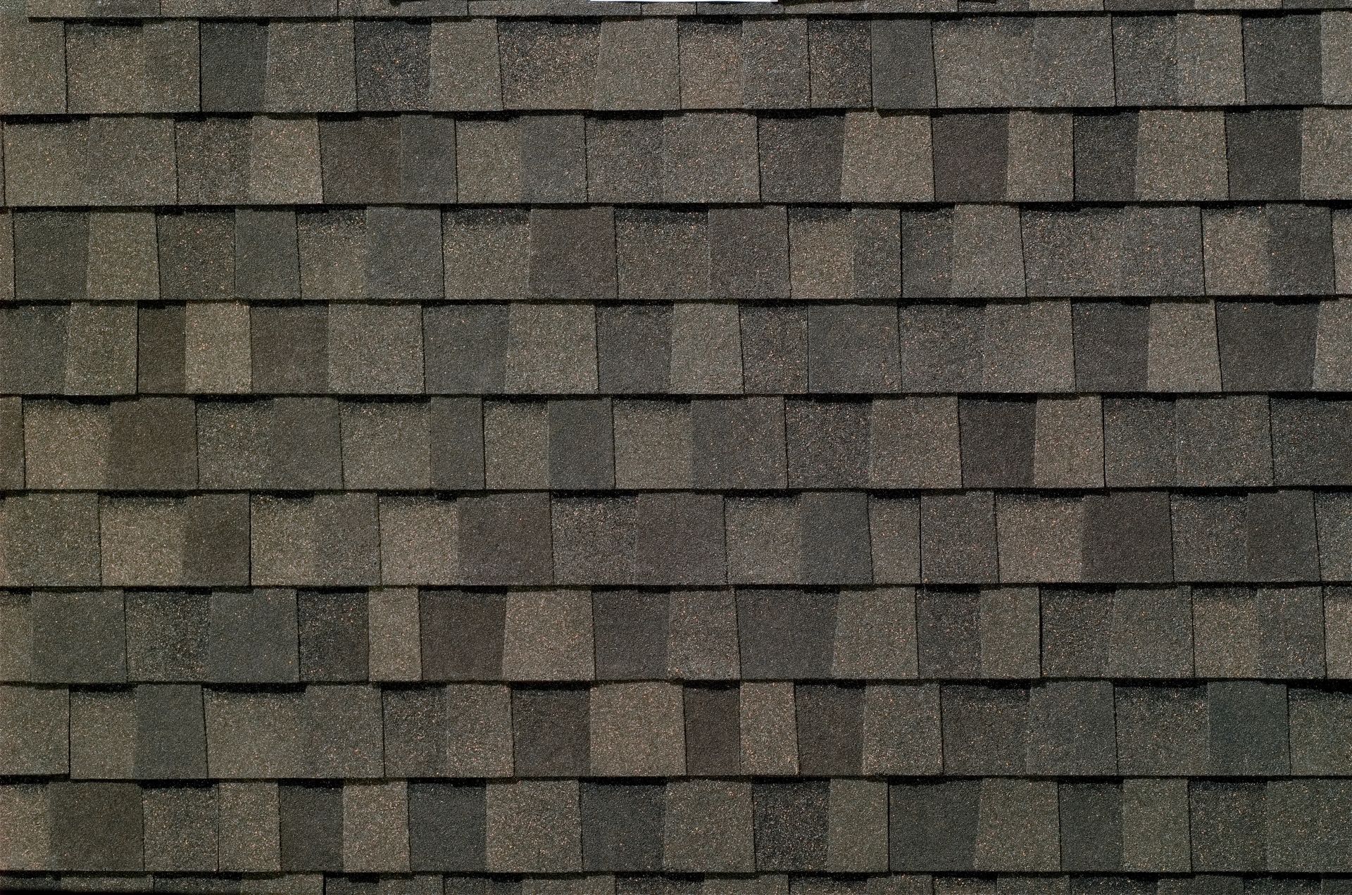 Close-up of a weathered gray-brown shingled roof with staggered rows of shingles.