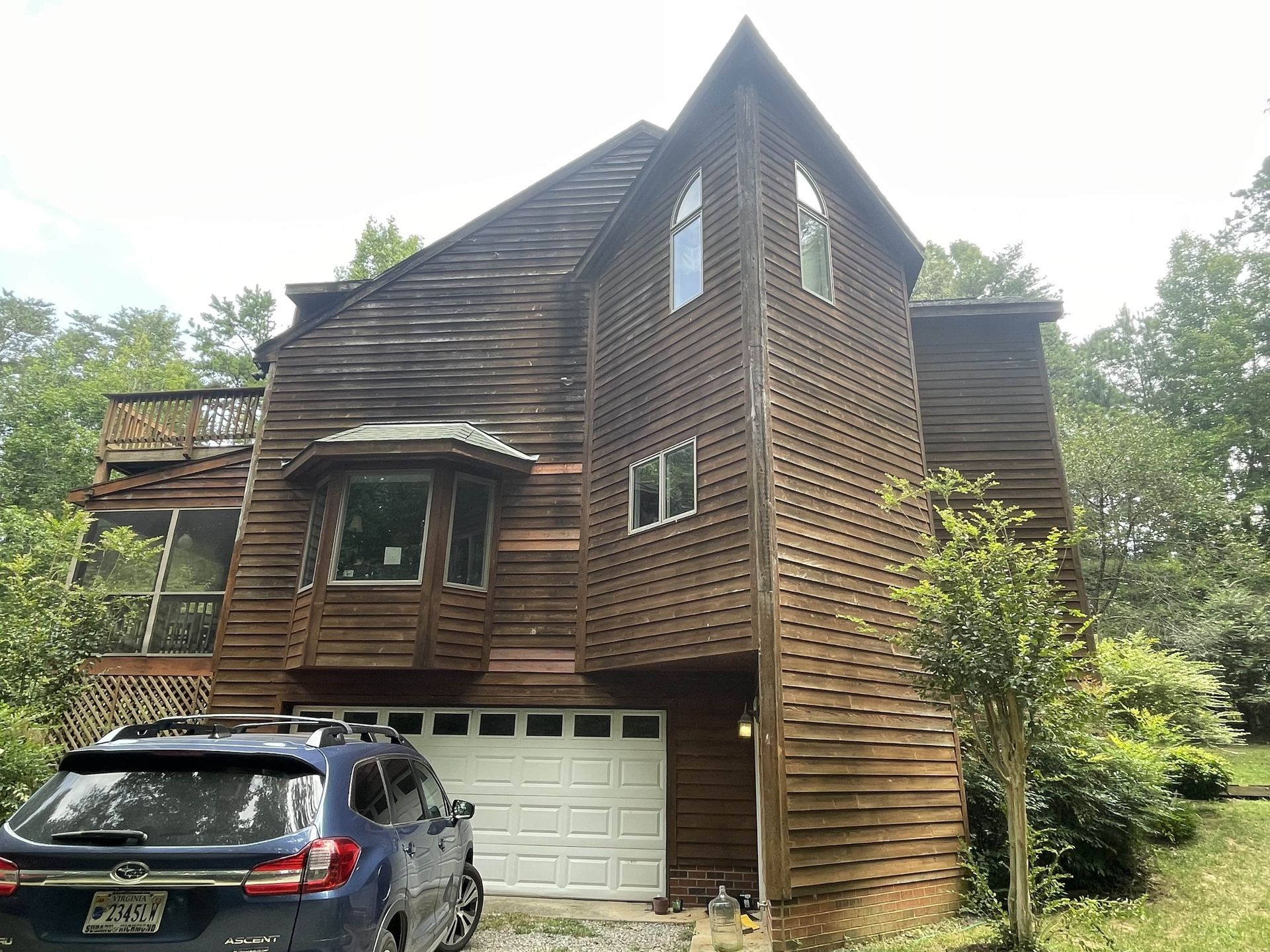Charred wooden house with garage, two parked cars, and trees after a fire