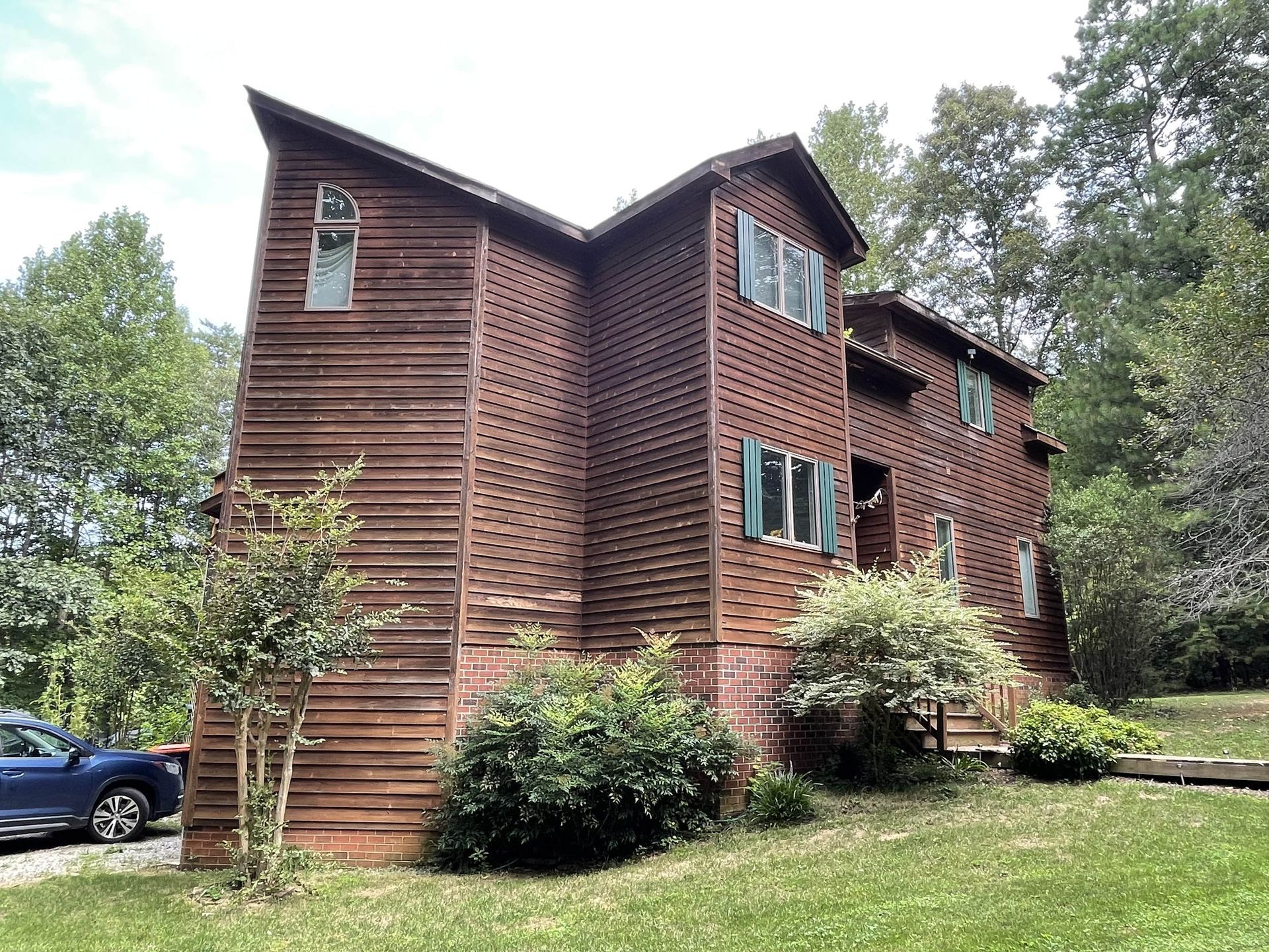 Three-story brick townhouse with green shutters, surrounded by trees and shrubs