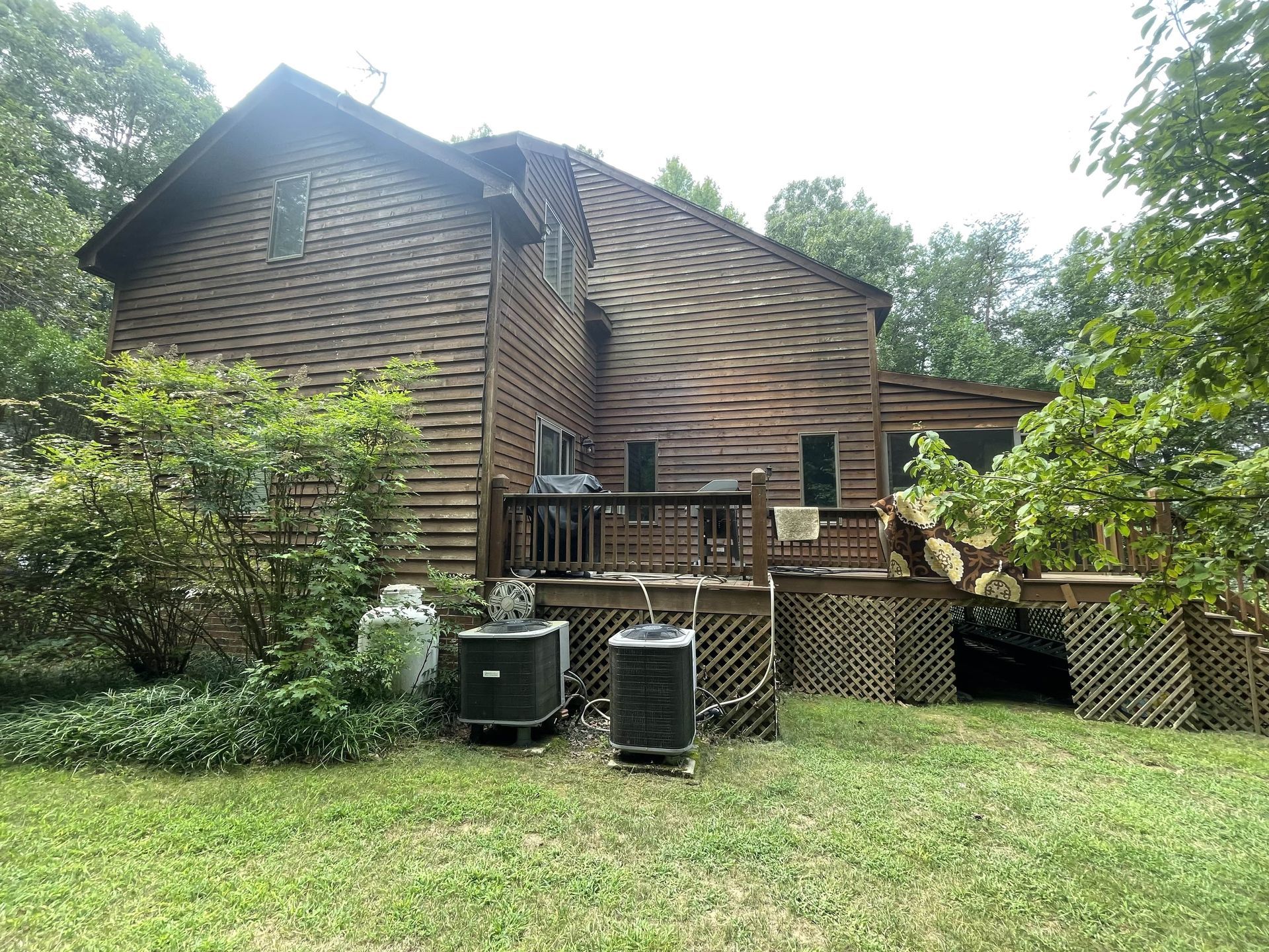 Log cabin with wooden deck and lattice skirting, surrounded by trees and a grassy yard.