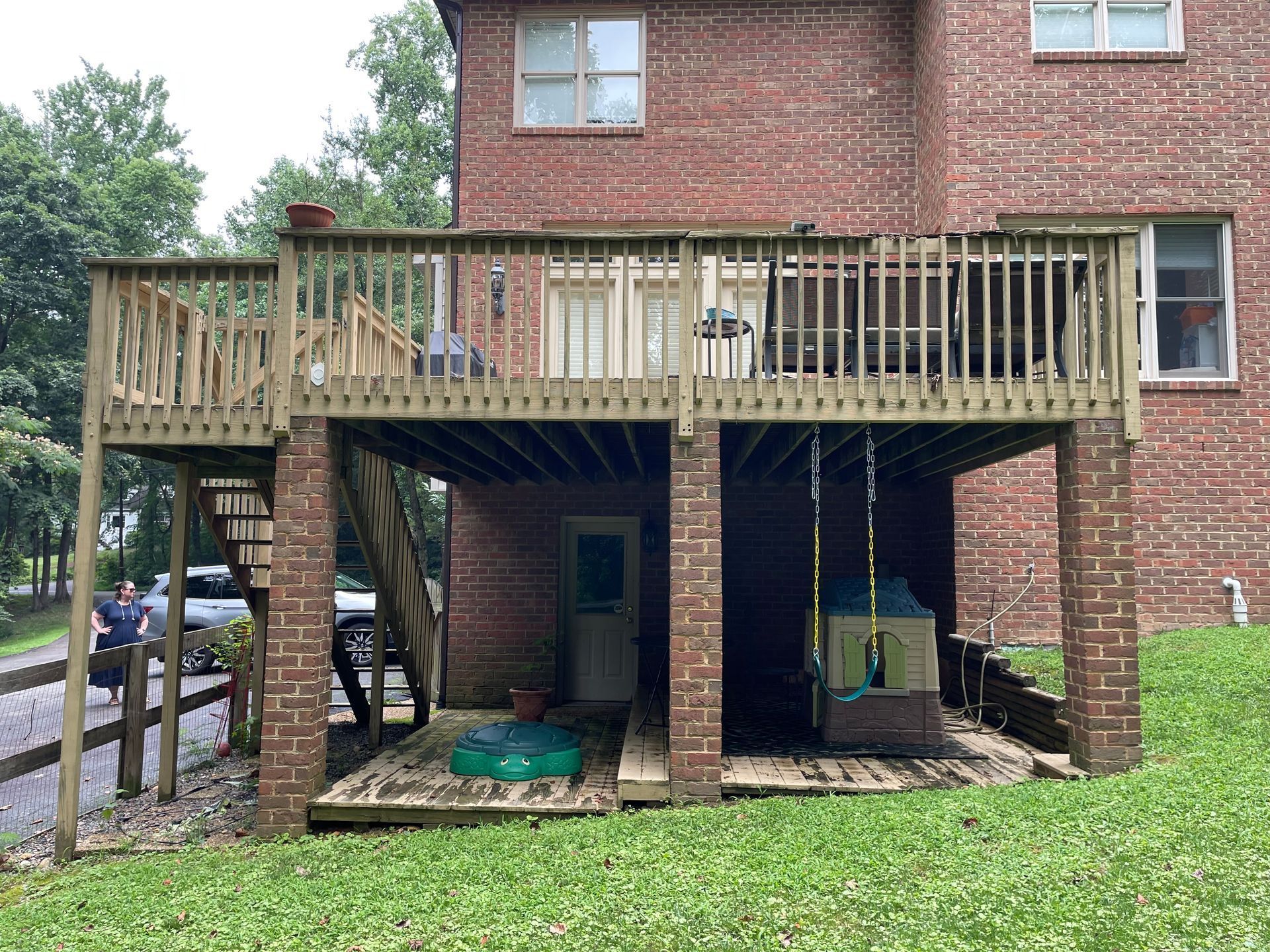 Backyard deck on a brick house with stairs, hanging swings, and grass below