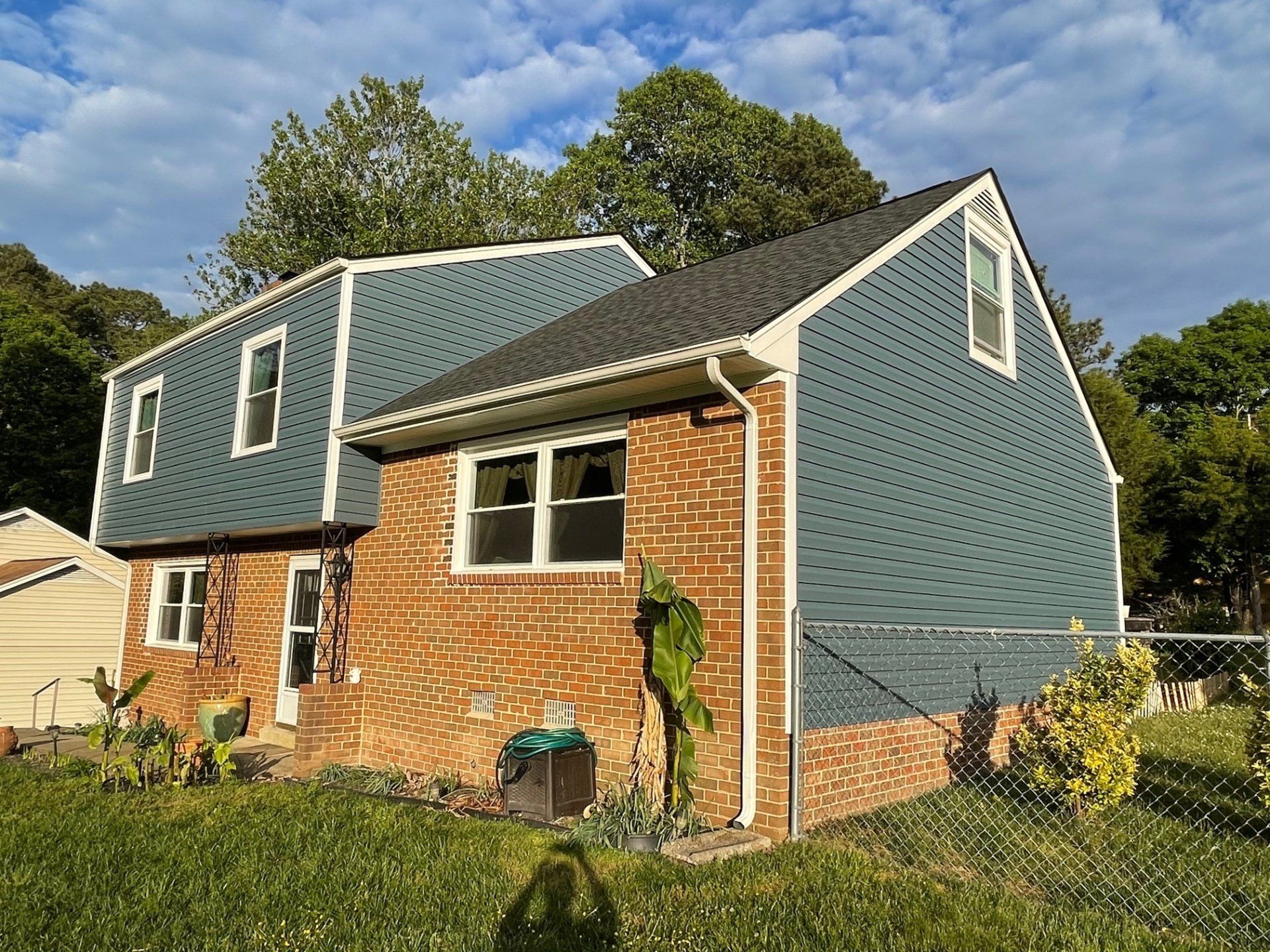 Brick house with blue shingle siding and white trim on a sunny day, seen from the yard