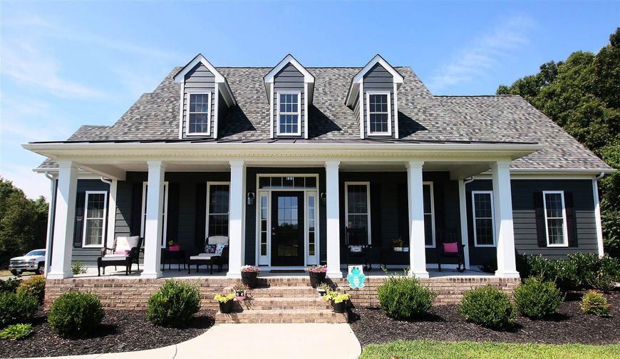 Two-story white house with black shutters, front porch, and dormer windows under a blue sky