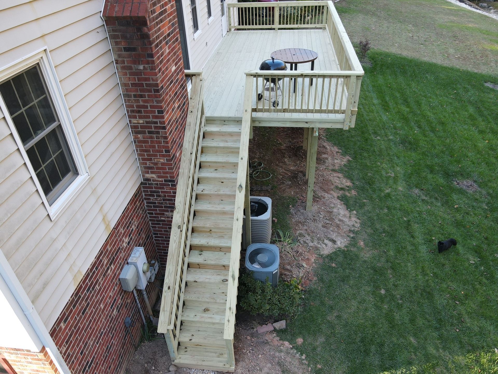 Wooden exterior stairs and landing beside a brick house, overlooking a grassy yard.