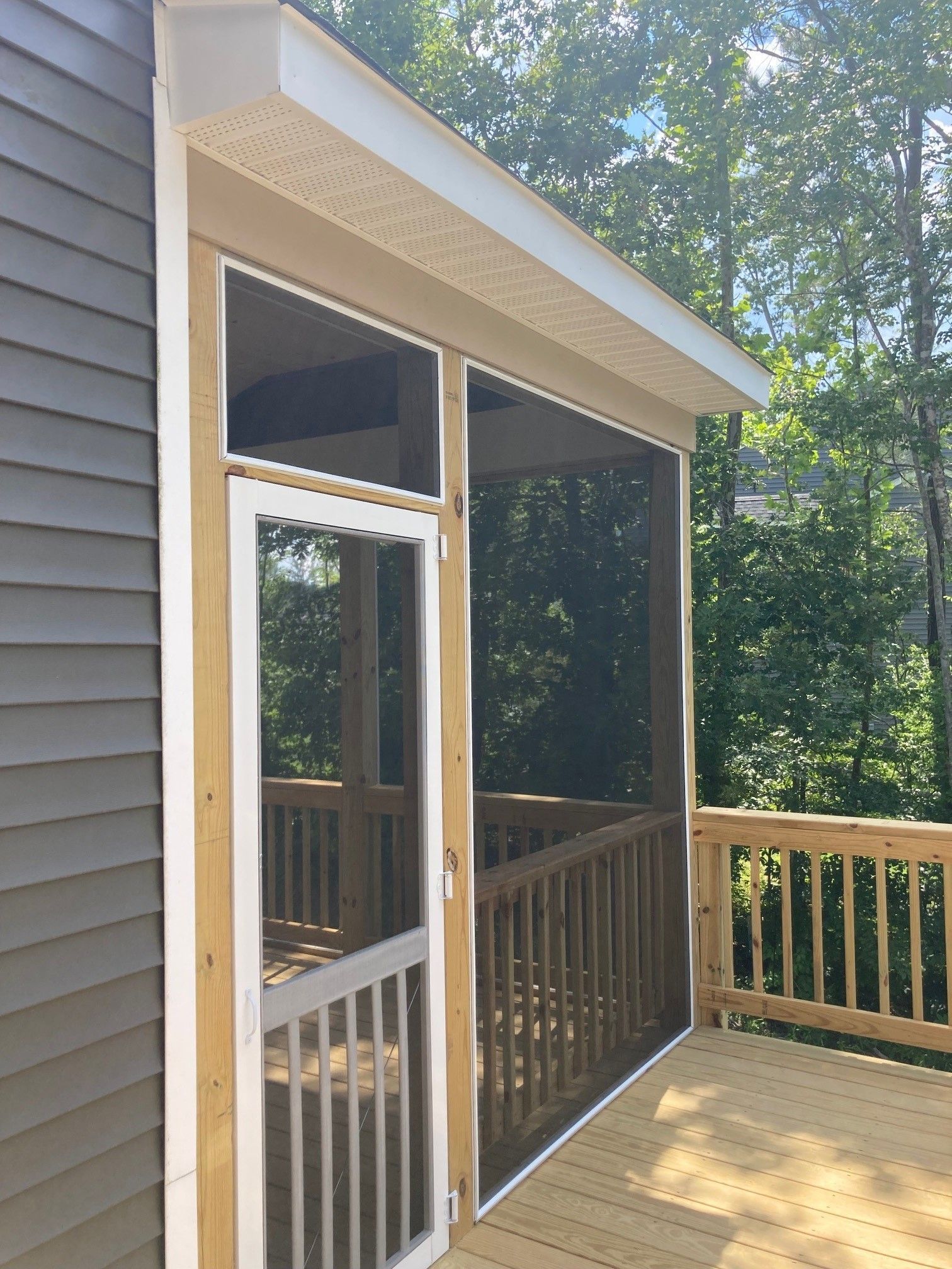 Covered backyard deck with white sliding glass door and railing, framed by trees and sunlight