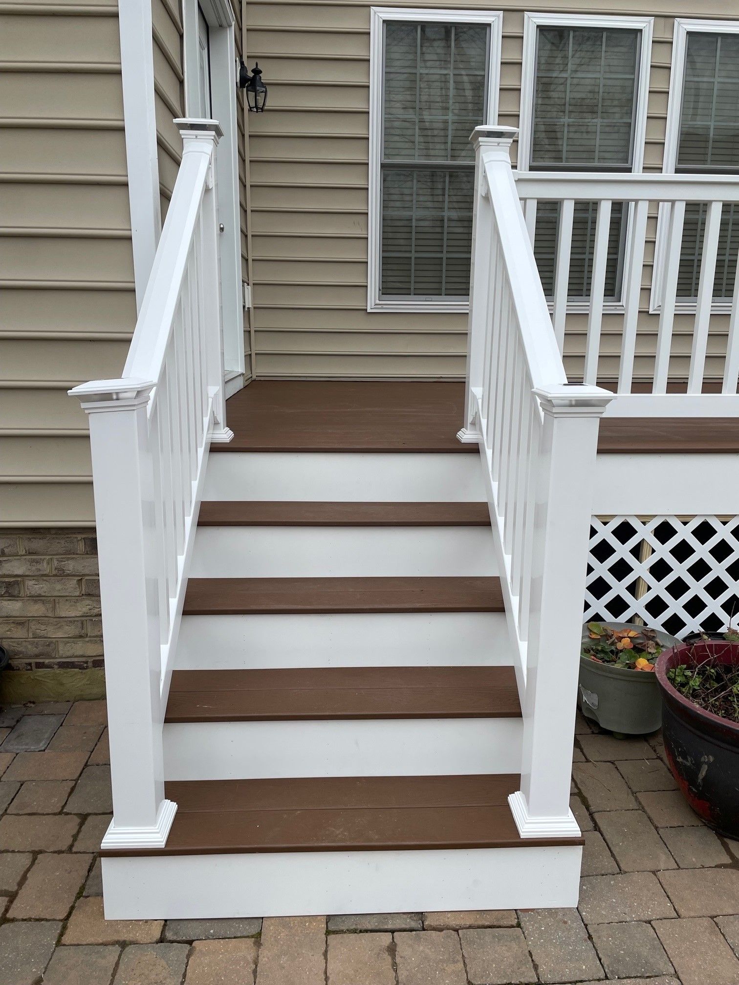 Front porch steps with white railings and brown treads leading to a beige house entrance.