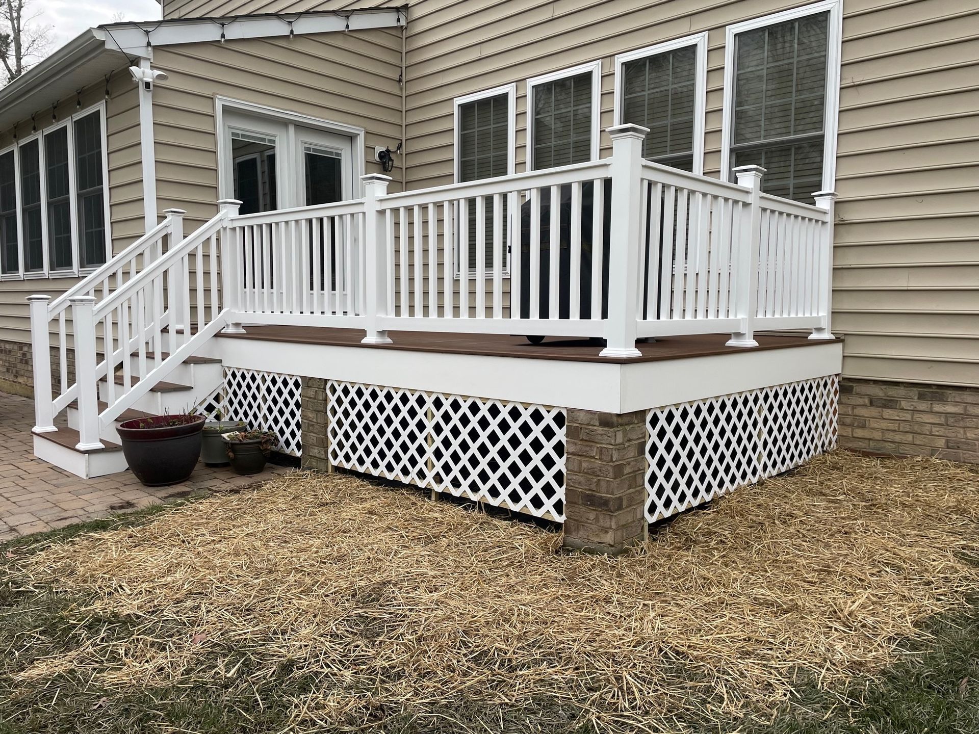 White deck with railings and lattice skirting attached to a beige house, beside a doorway and patio pot