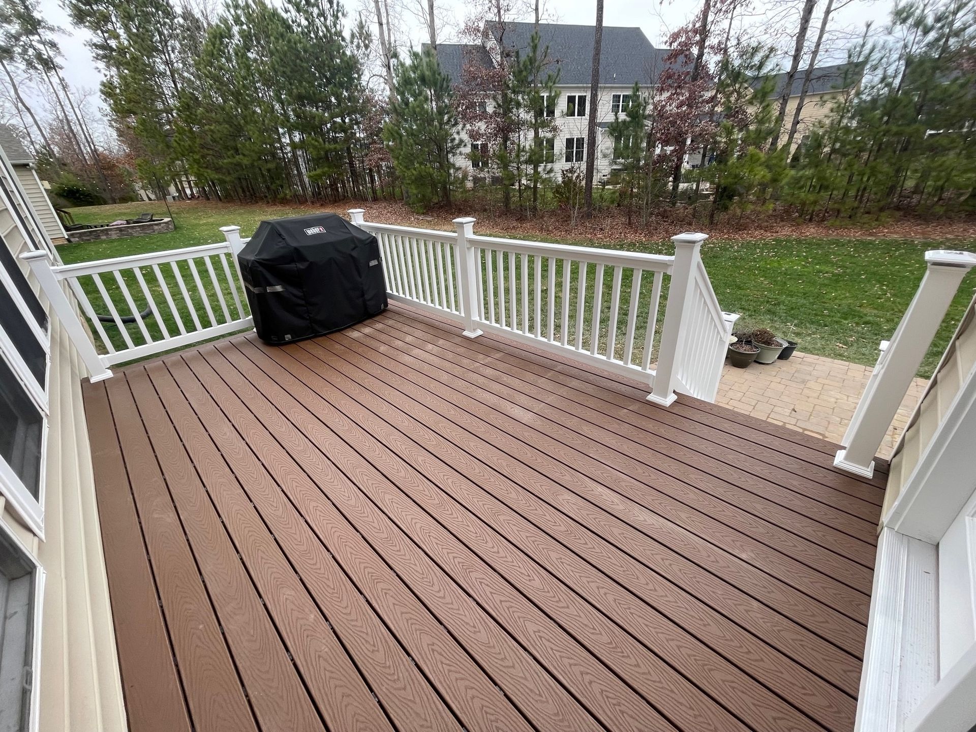 Wooden deck with white railings and a covered grill, overlooking a grassy yard and house.