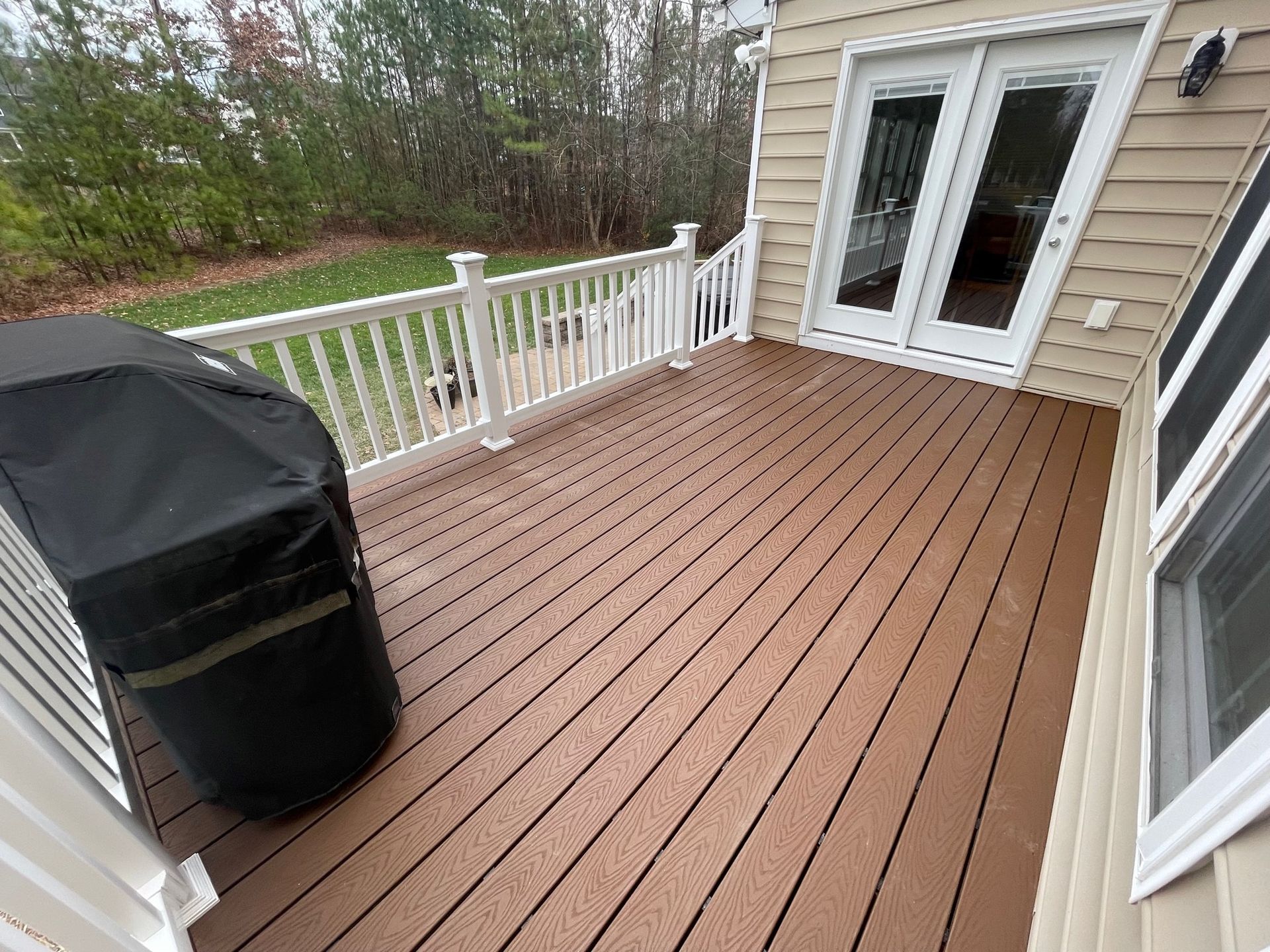 Wooden deck with white railing, black grill cover, and glass patio doors leading to a house