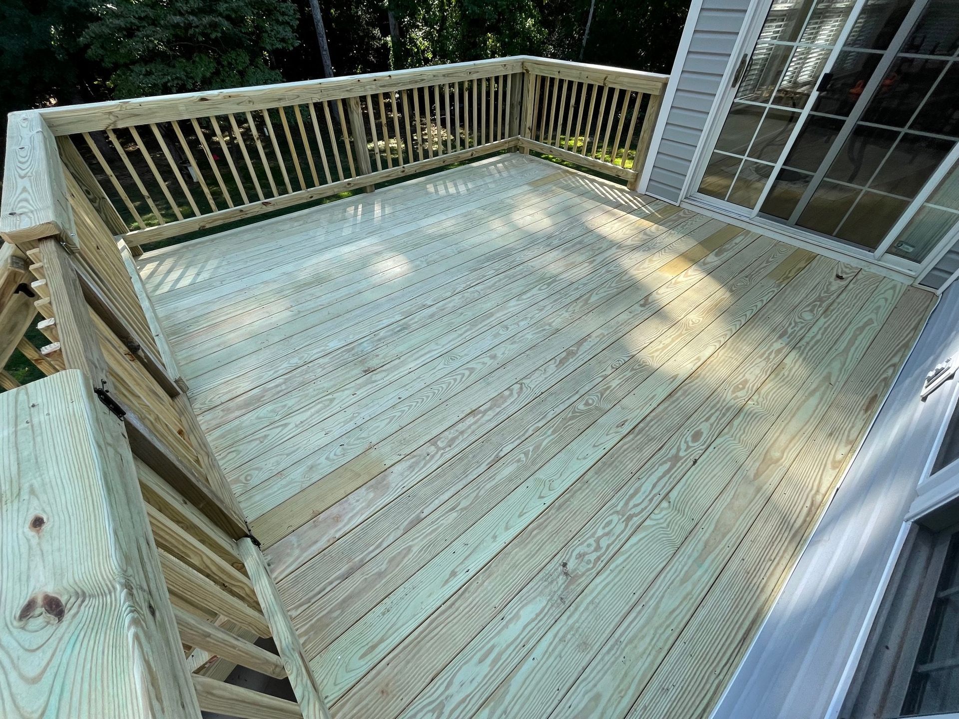 Wooden backyard deck with railings and stairs, viewed from the house.
