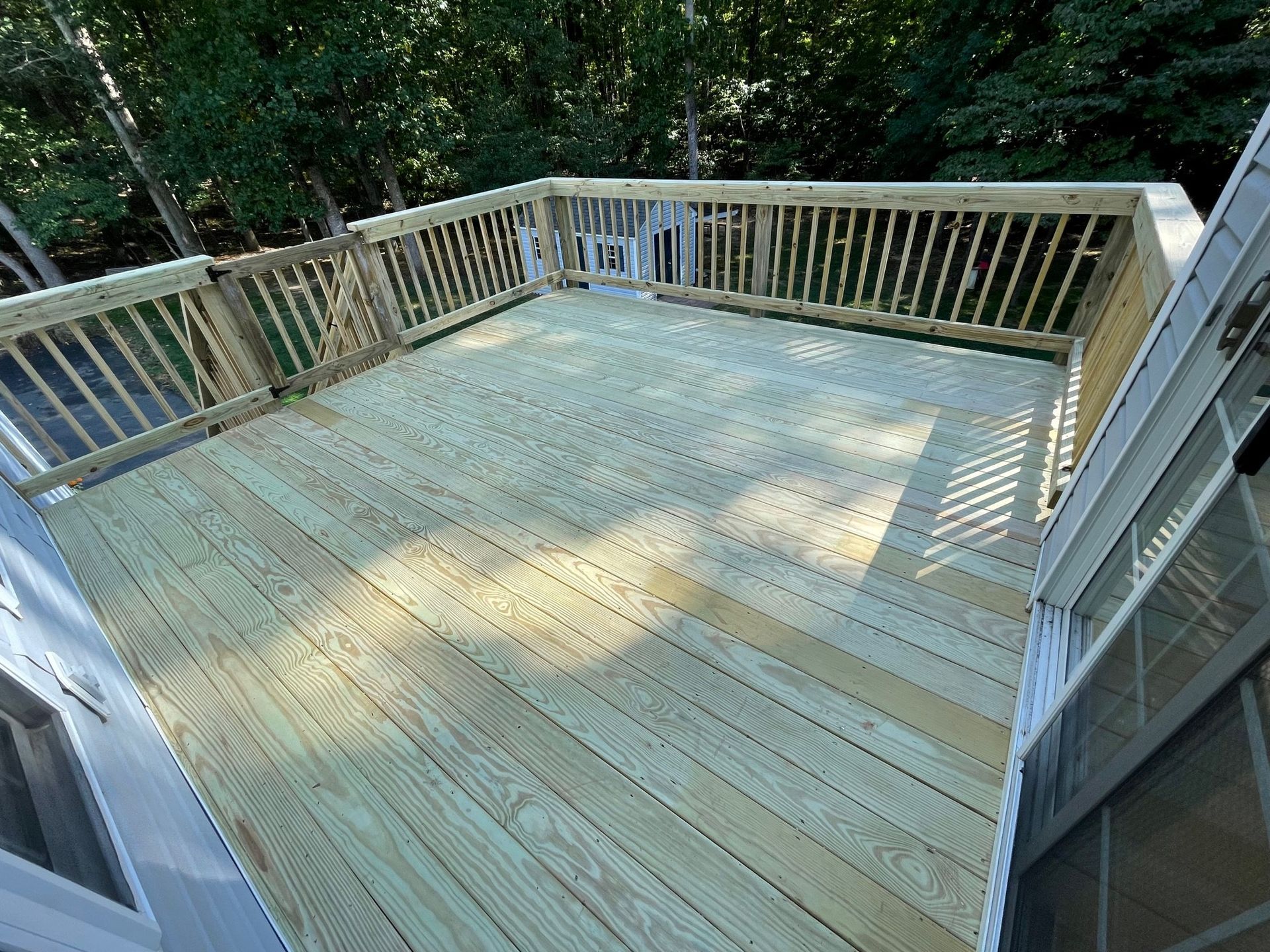 Wooden deck with white railings in a wooded backyard, sunlit and empty