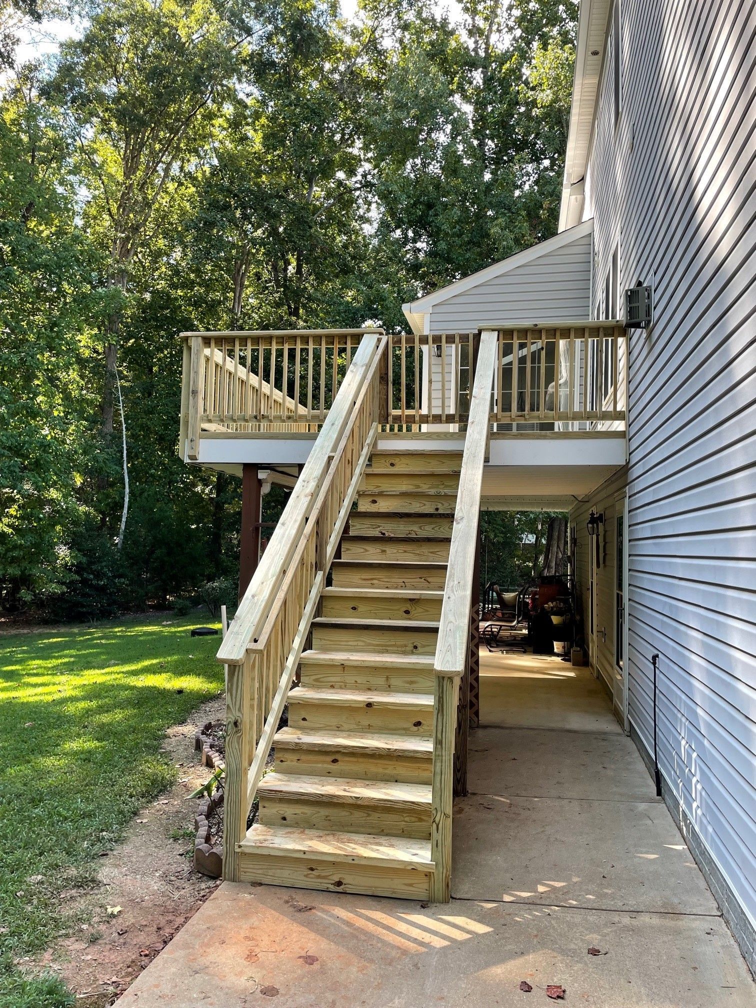 Wooden exterior staircase leading to an elevated deck beside a house, with a concrete walkway below.