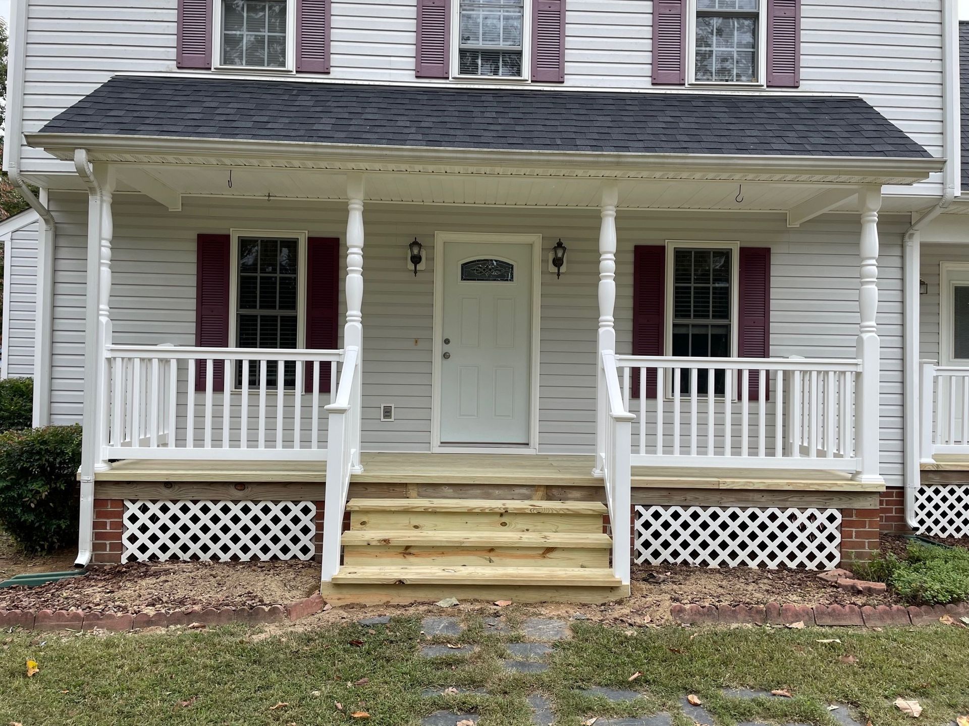 Front porch of a gray house with white railings, red shutters, and brick steps.