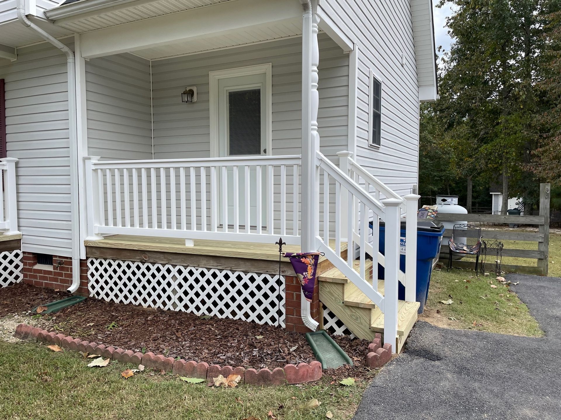 Front porch with white railing and steps, showing a yellow handrail ramp on a gray house.
