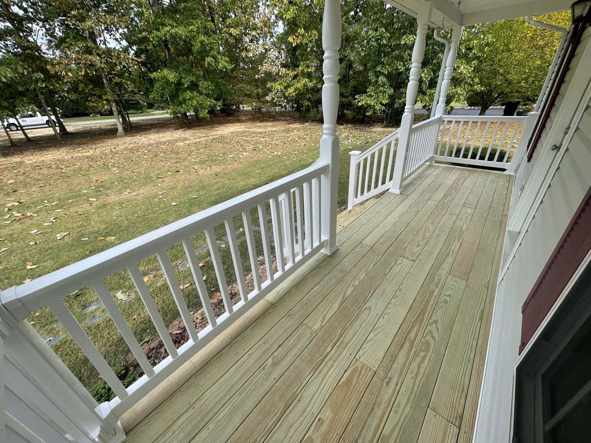 Covered front porch with white railings and tan wooden floor overlooking a grassy yard.