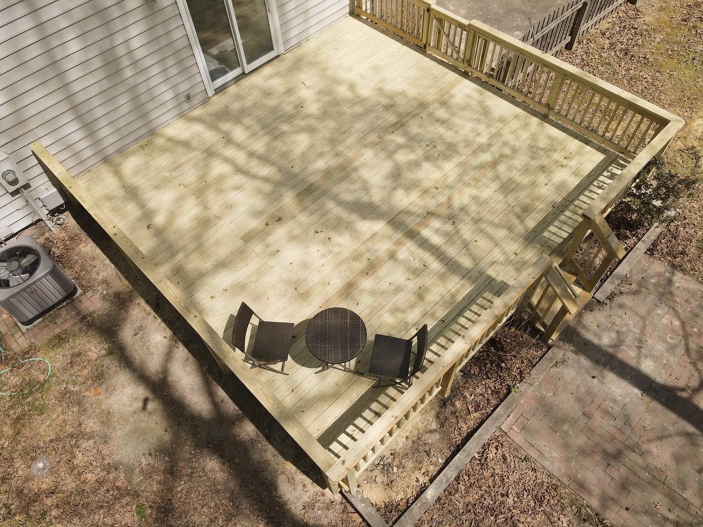 Overhead view of a wooden deck with a table and chair in a fenced backyard.