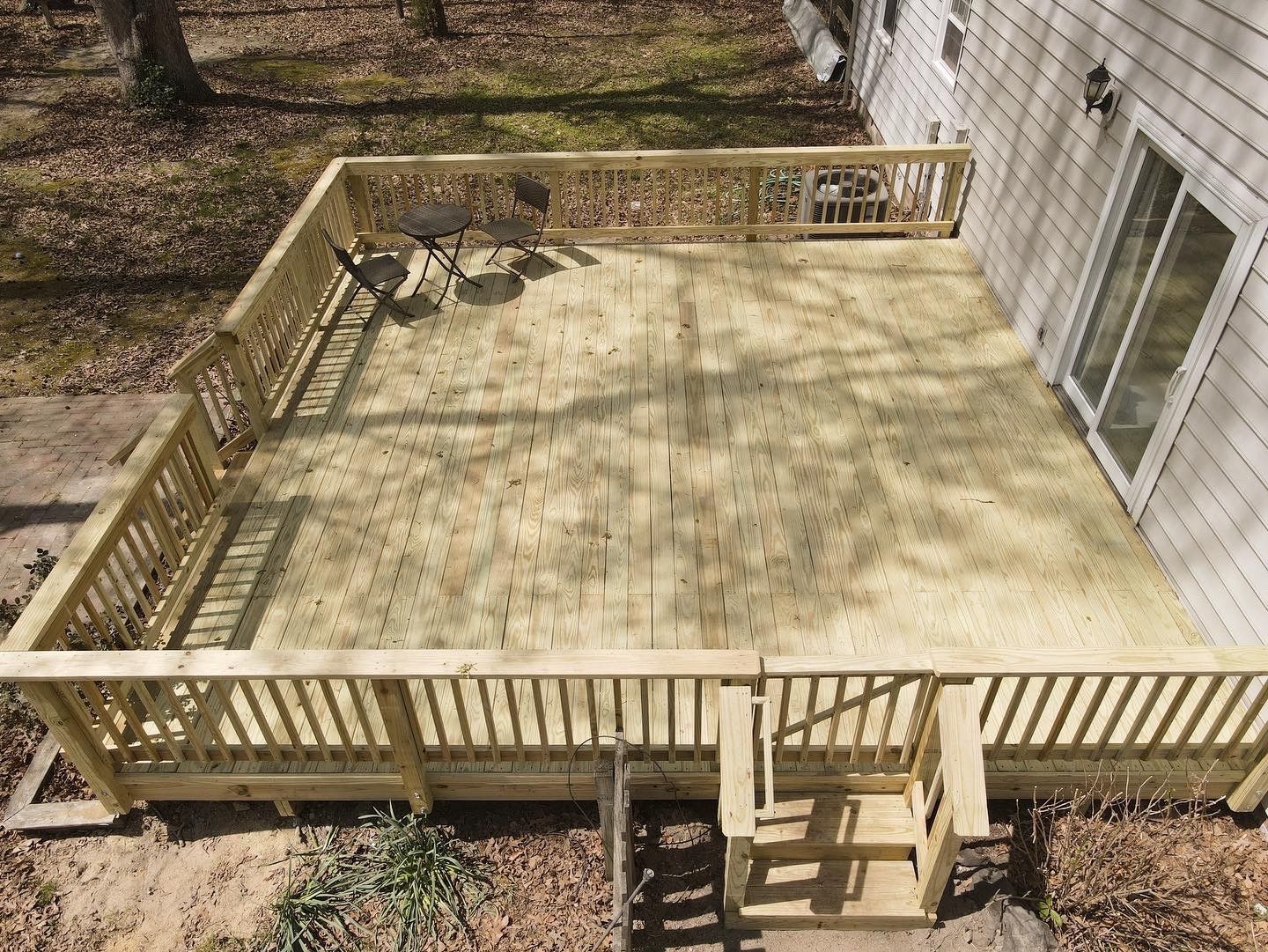 Wooden backyard deck with railings and stairs beside a house, with a table and chairs in one corner.