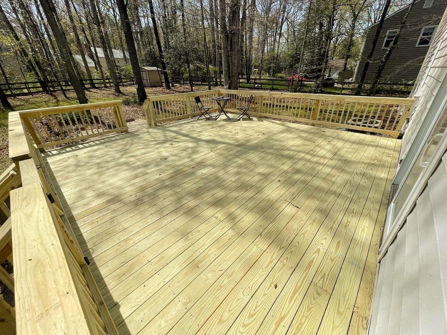 Sunlit wooden backyard deck with railings, surrounded by trees and a house