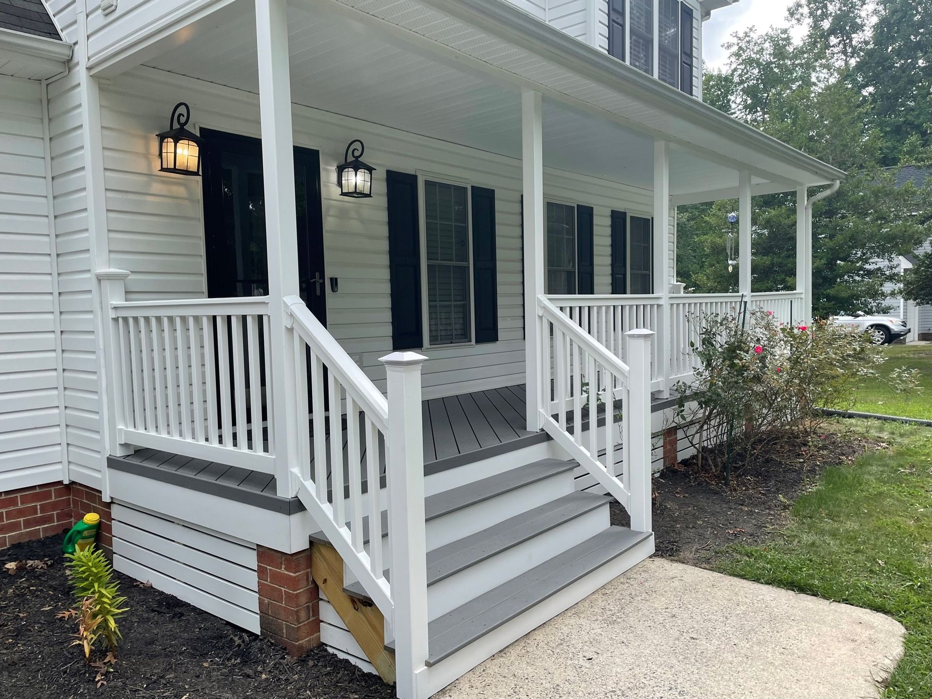 Front porch with white railings and gray steps on a white house with black shutters and lantern lights