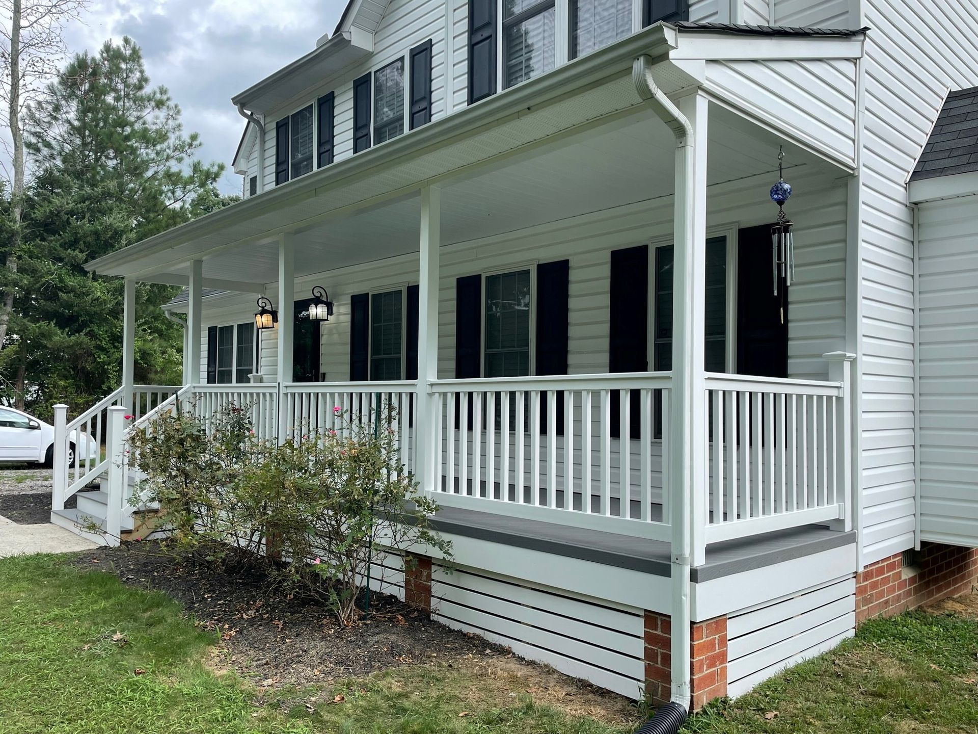 White house porch with railing and steps, covered by a roof and surrounded by a lawn.