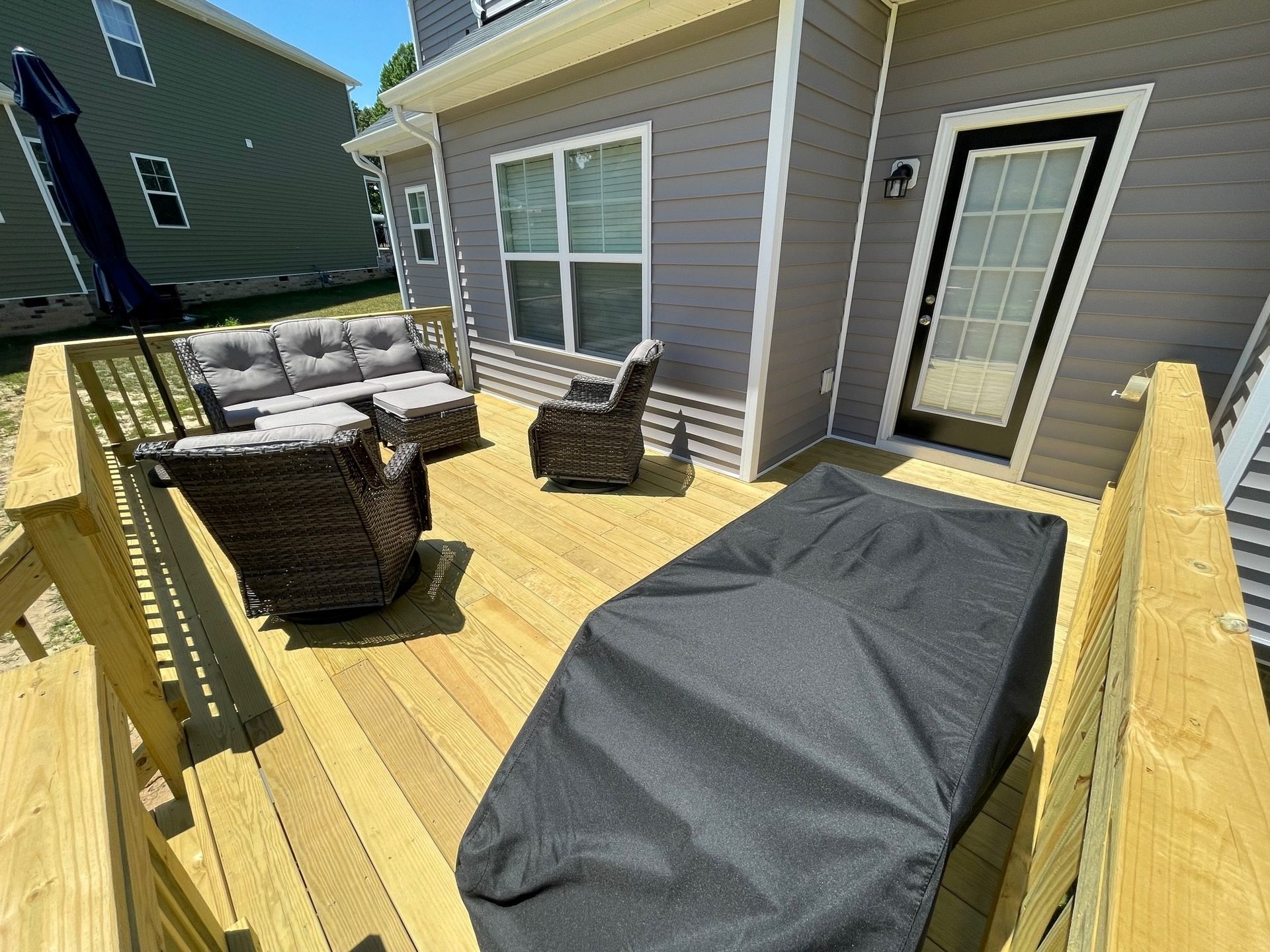 Back deck with wicker seating, grill, and a covered item beside a house with sliding glass doors
