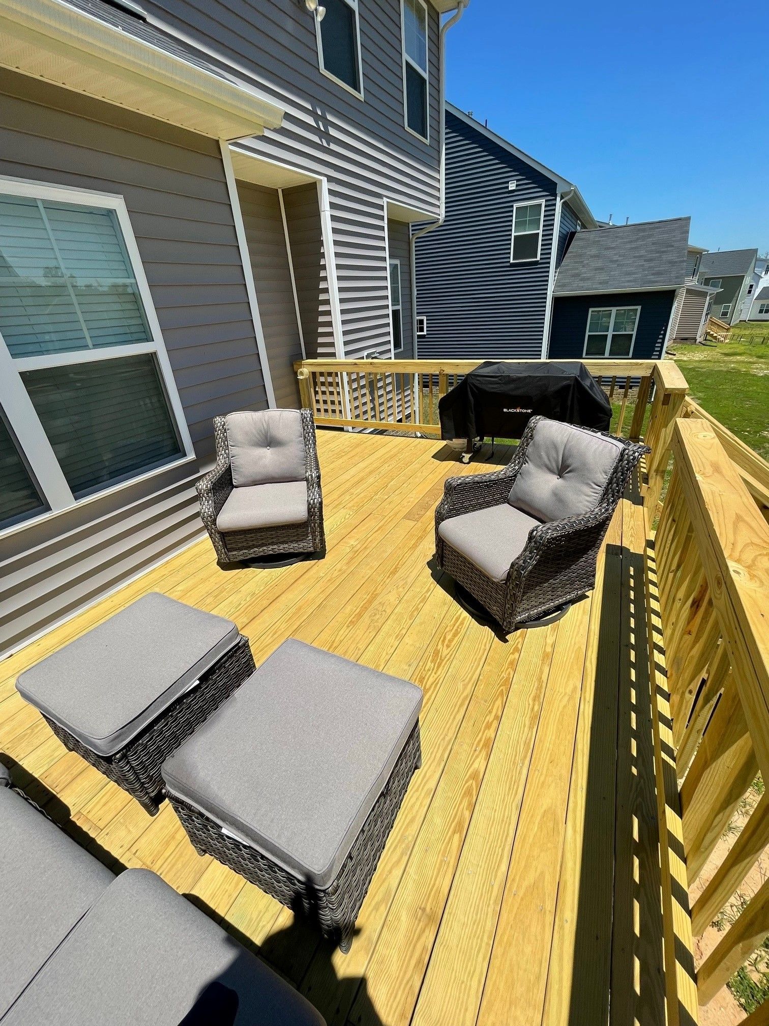 Back deck with yellow flooring, gray patio chairs, lounge cushions, and a black grill beside the house