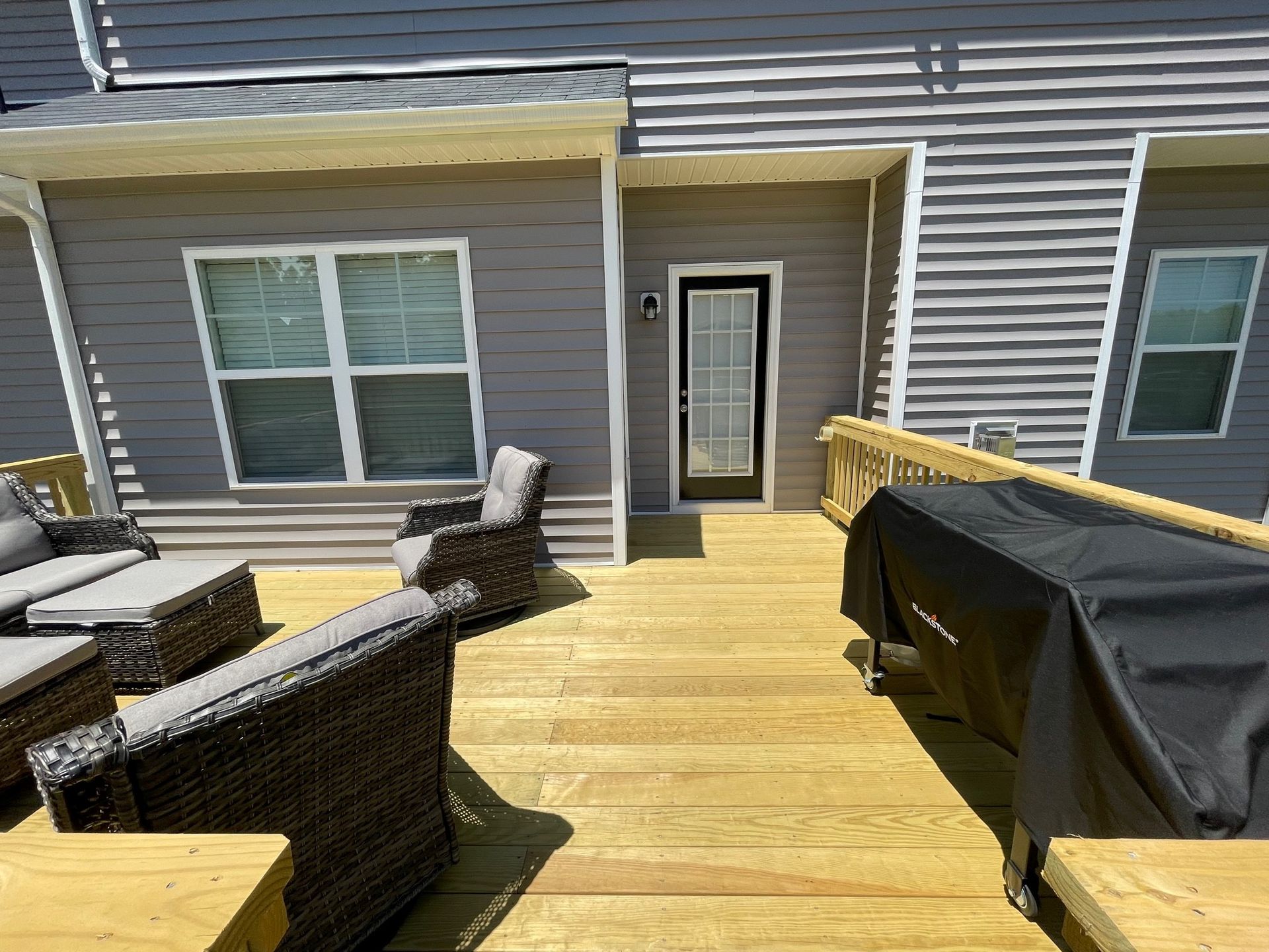 Back deck with wicker chairs and a grill beside gray house siding and a glass patio door