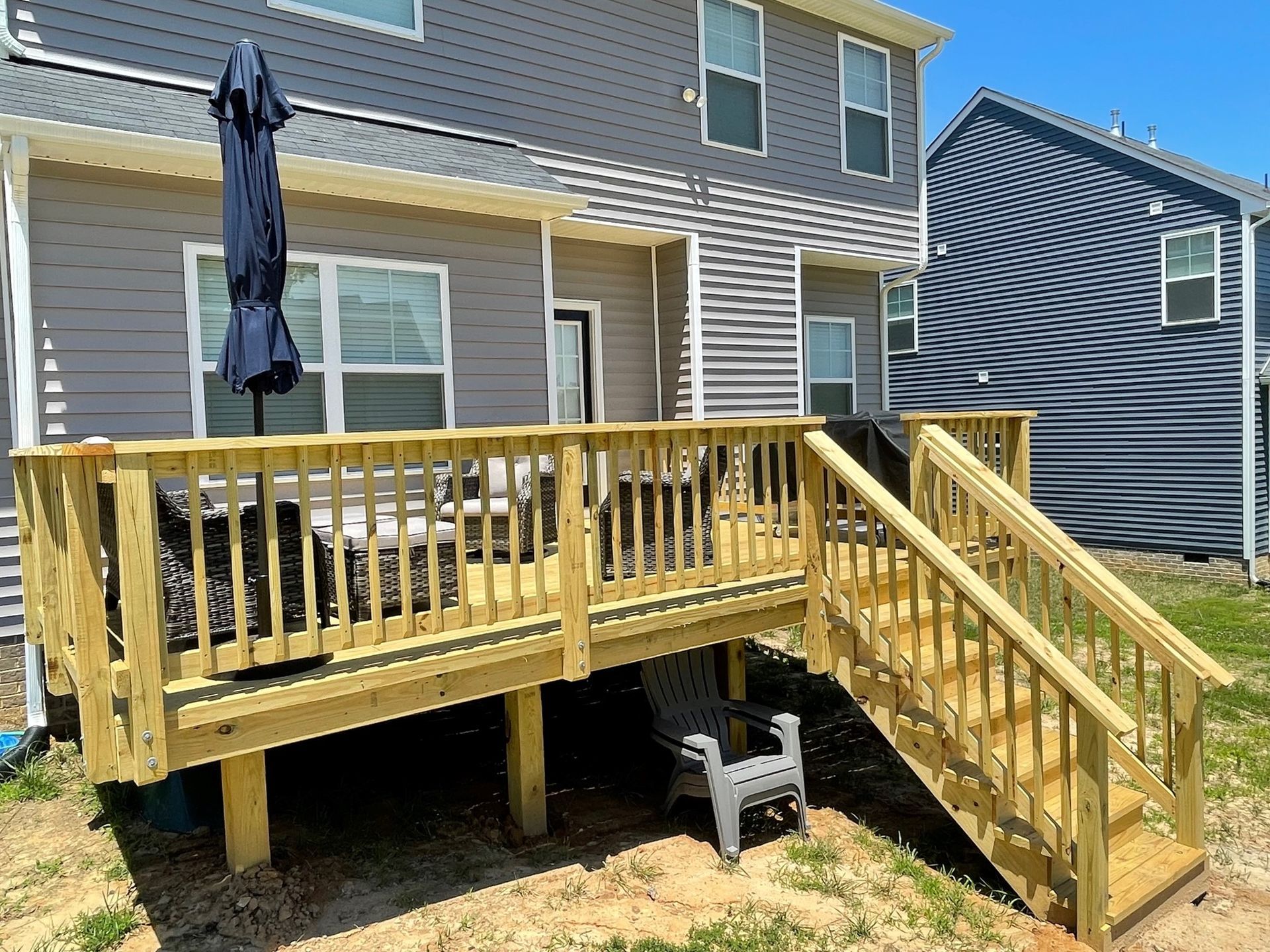 Wooden backyard deck with stairs beside a house, yellow railings, and a closed patio umbrella